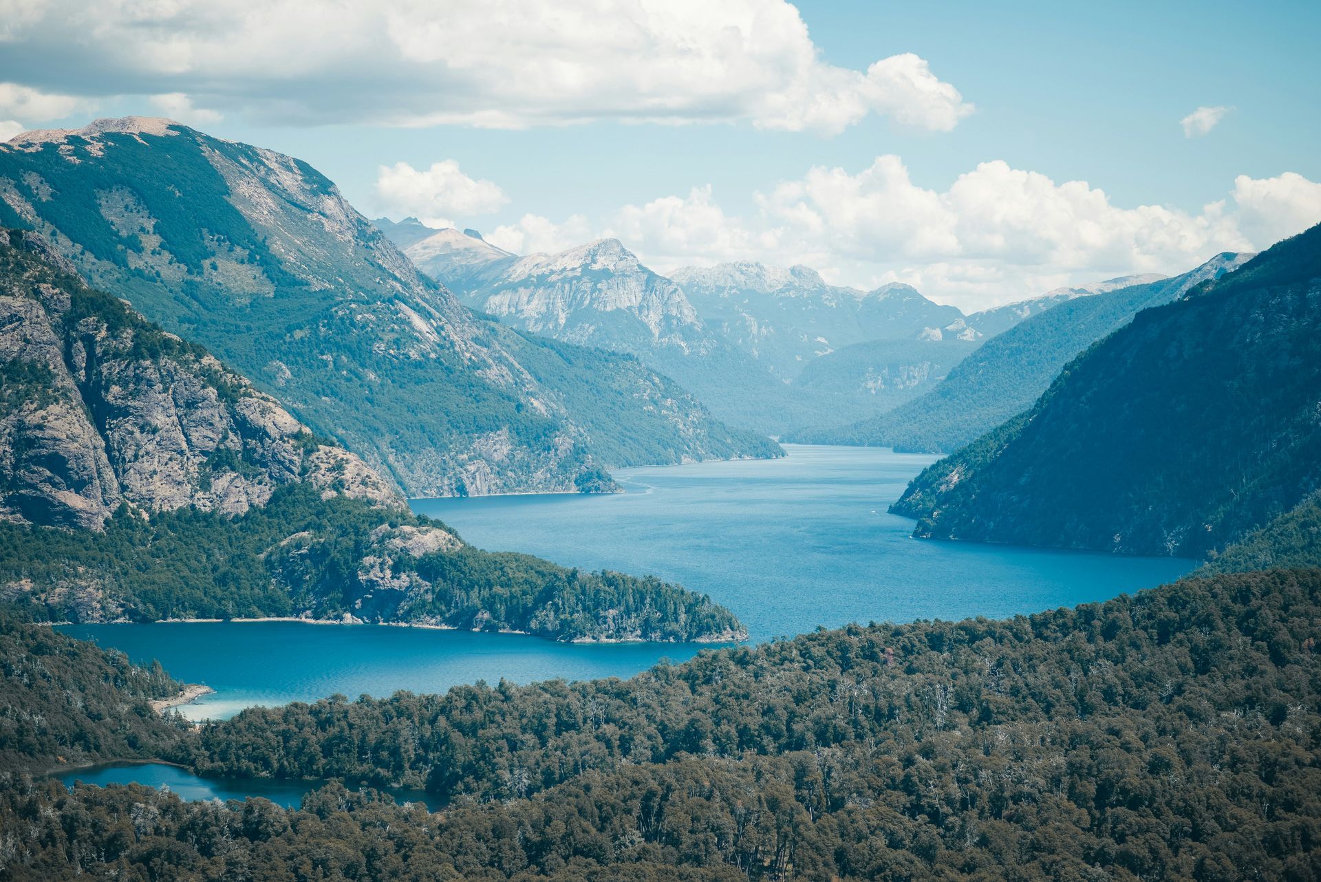 Lush green mountains surround a blue lake under a partly cloudy sky in Patagonia, Argentina.