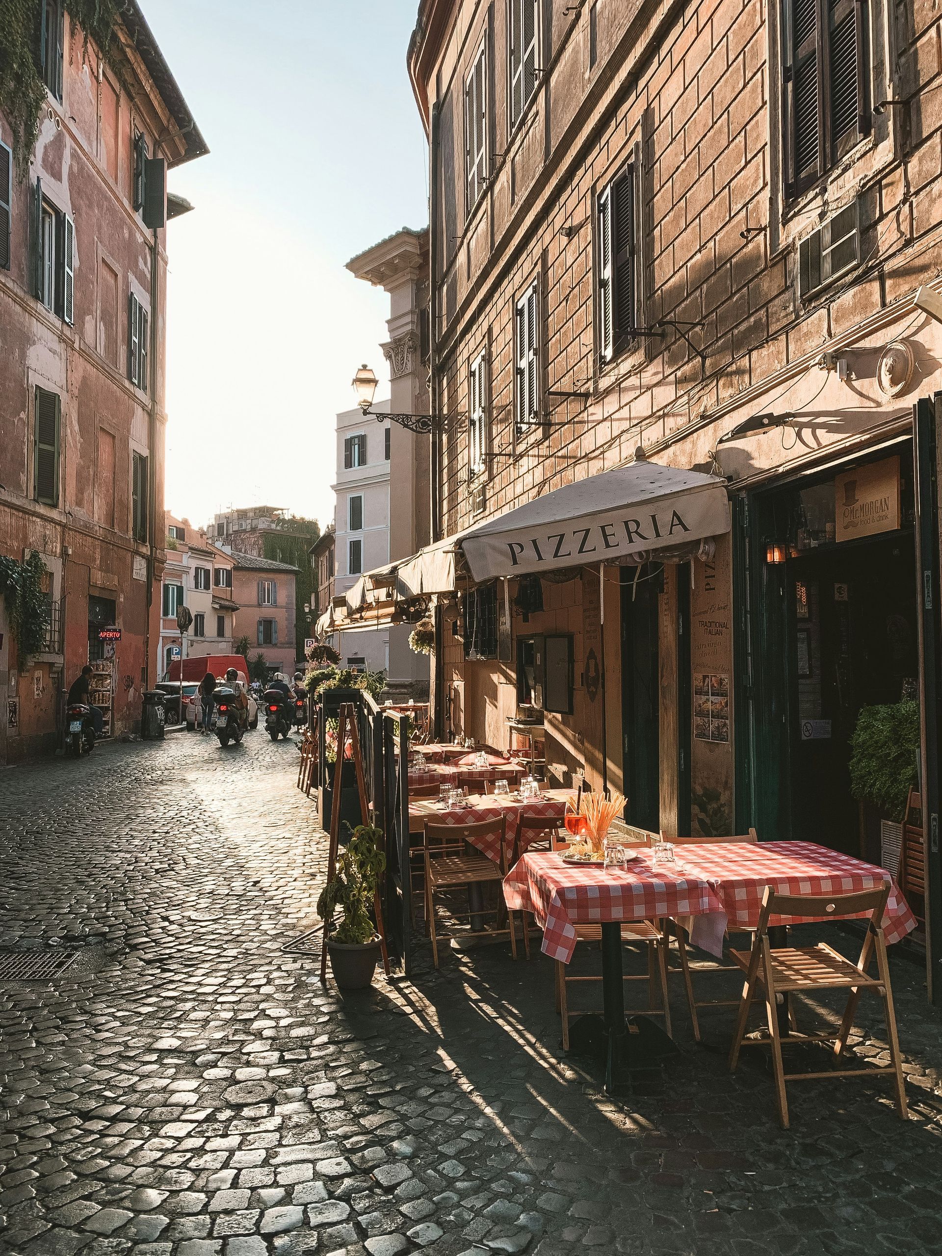 A cobblestone street with tables and chairs in front of a pizzeria in Rome.