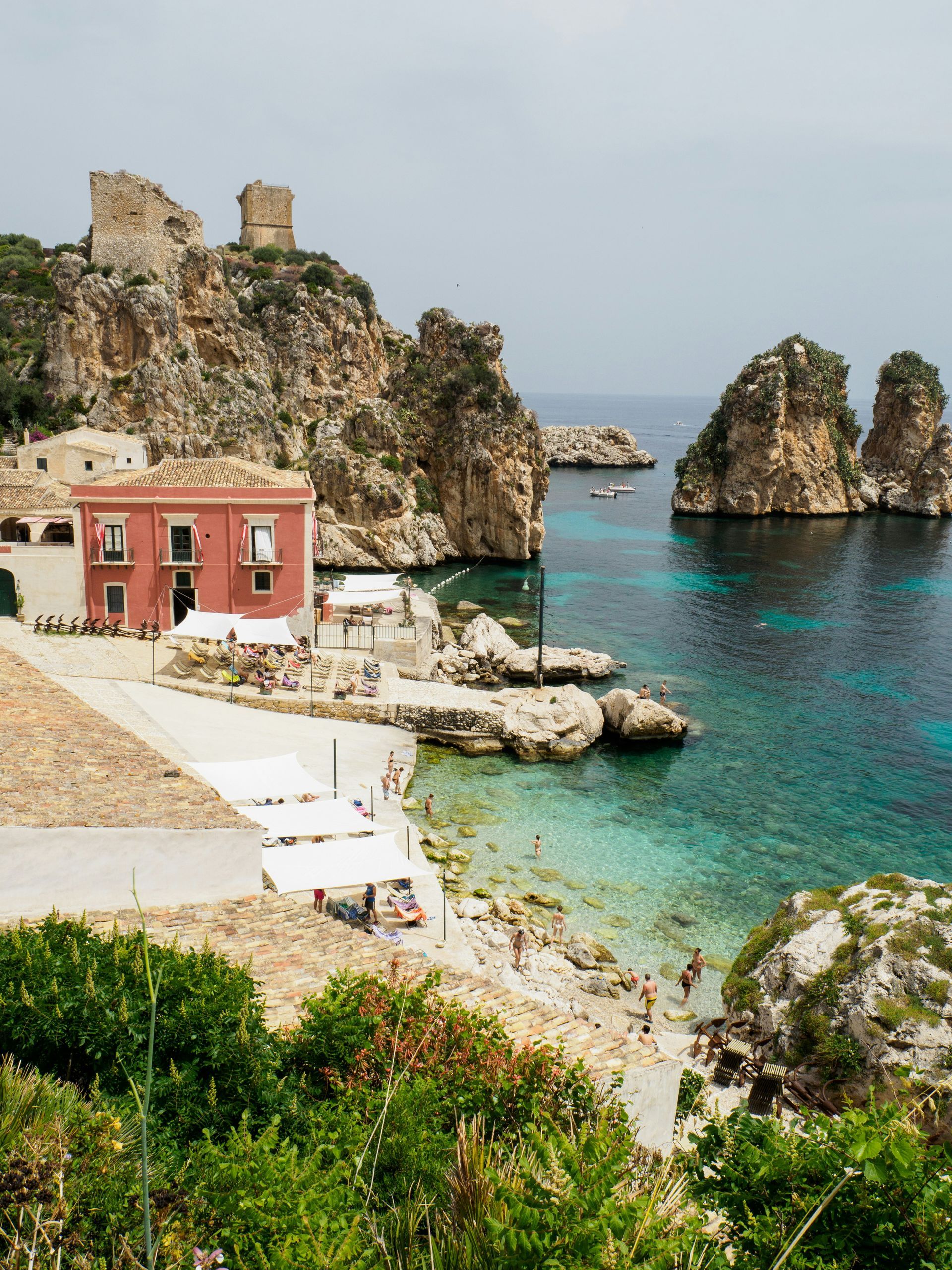 A beach with a red building in the foreground and a body of water in the background in Sicily.