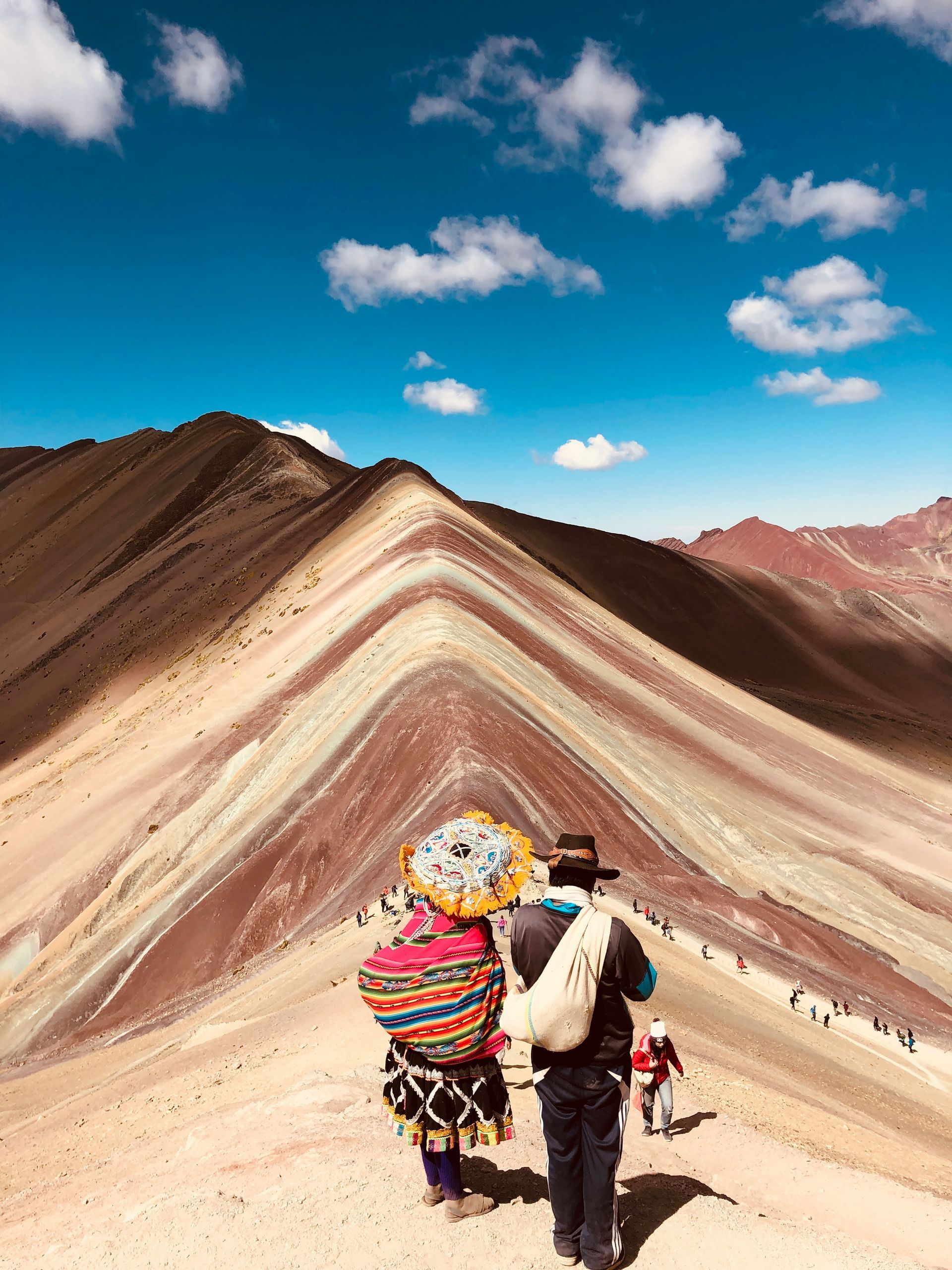 A man and a woman are walking up the rainbow mountains of Vinicunca, Peru.