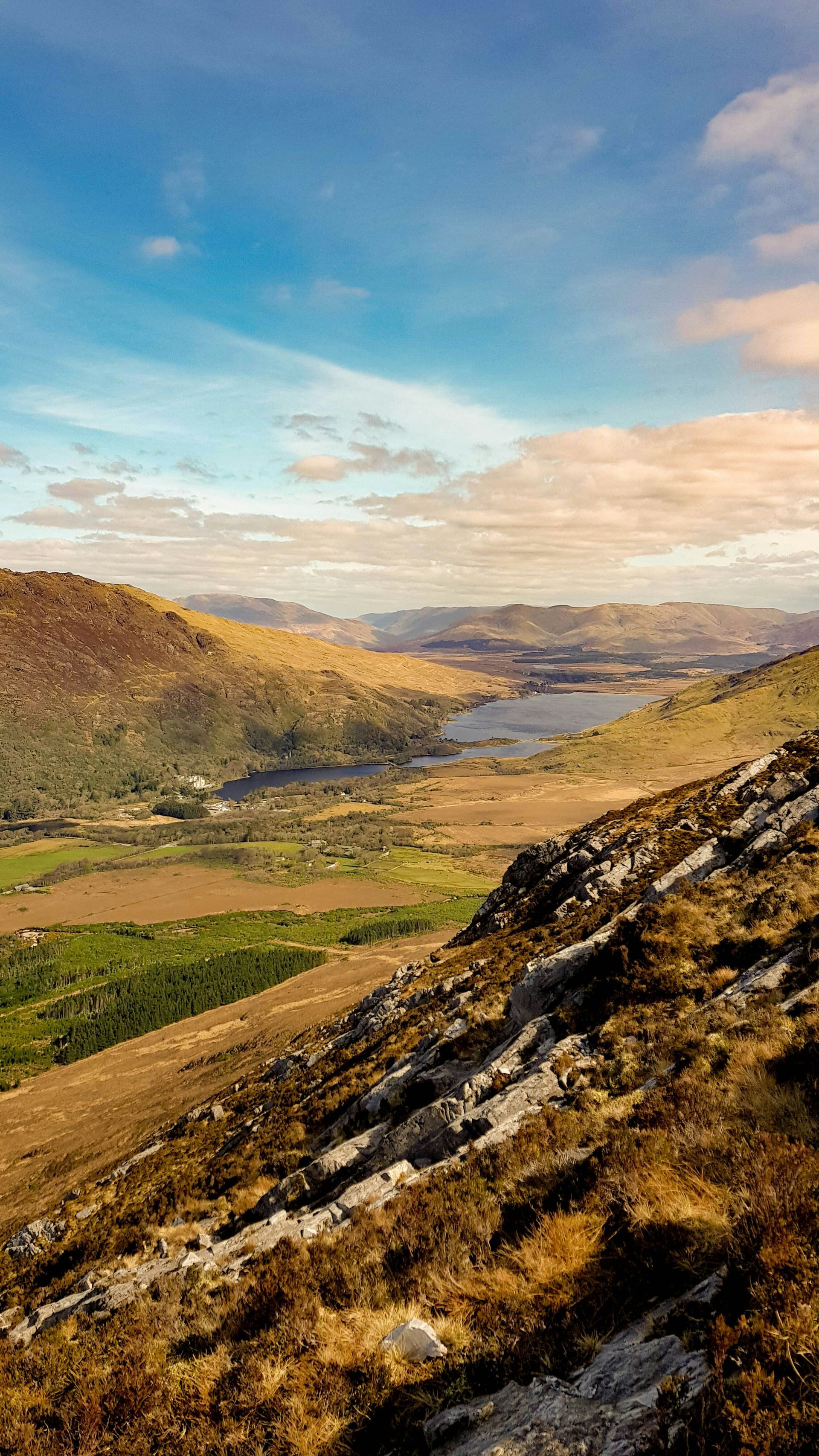 Rolling hills with a valley, lake, and cloudy sky. Golden and green hues dominate landscape in Connemara, Ireland.