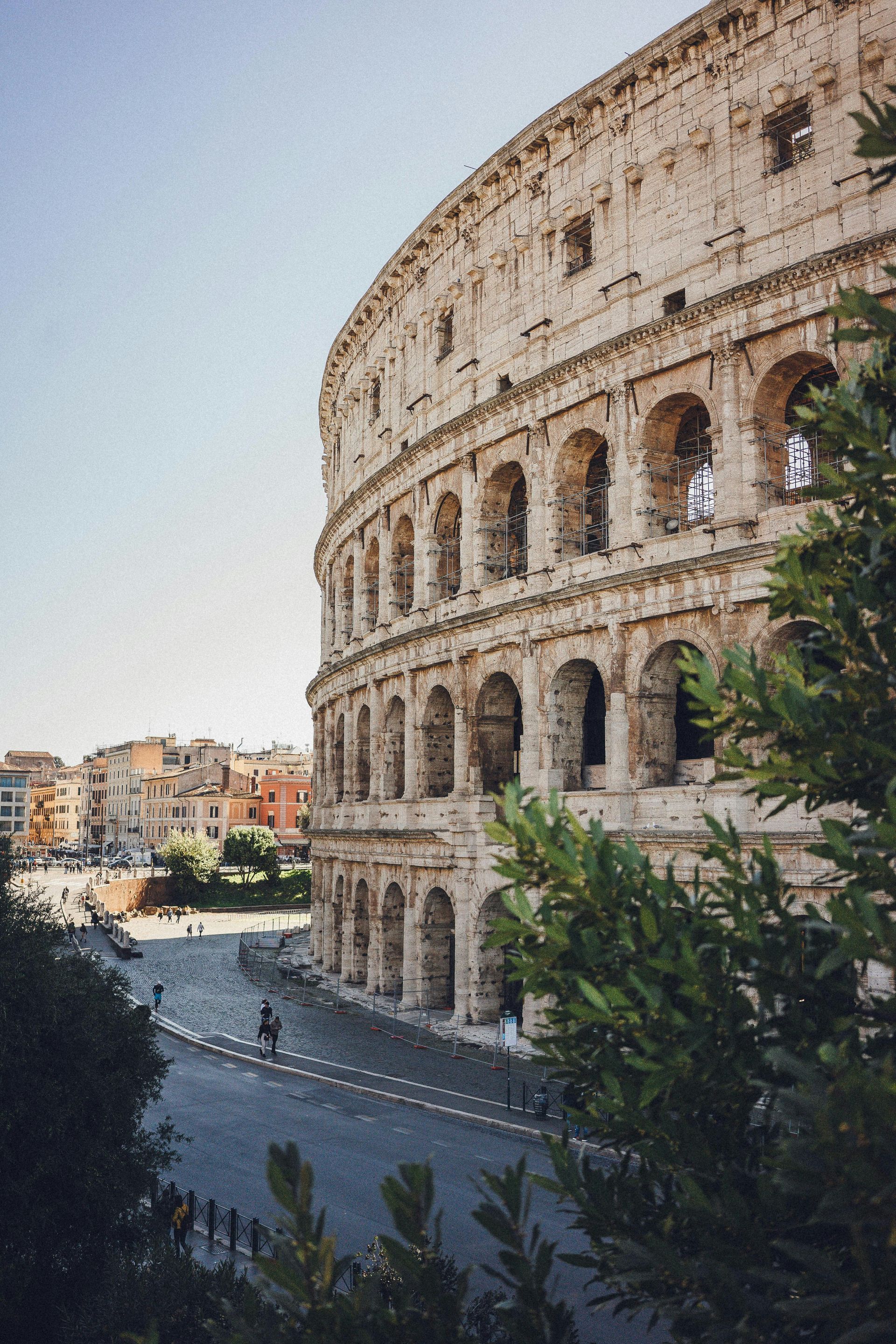 The colosseum in Rome is surrounded by trees and a street.
