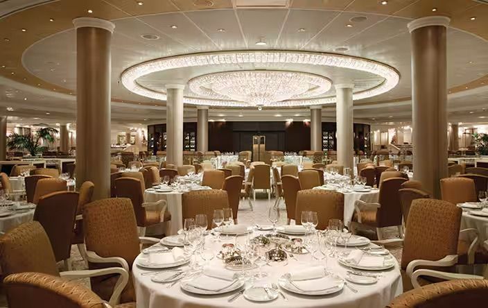 A large dining room filled with tables and chairs and a chandelier on the Oceania Marina cruise ship.