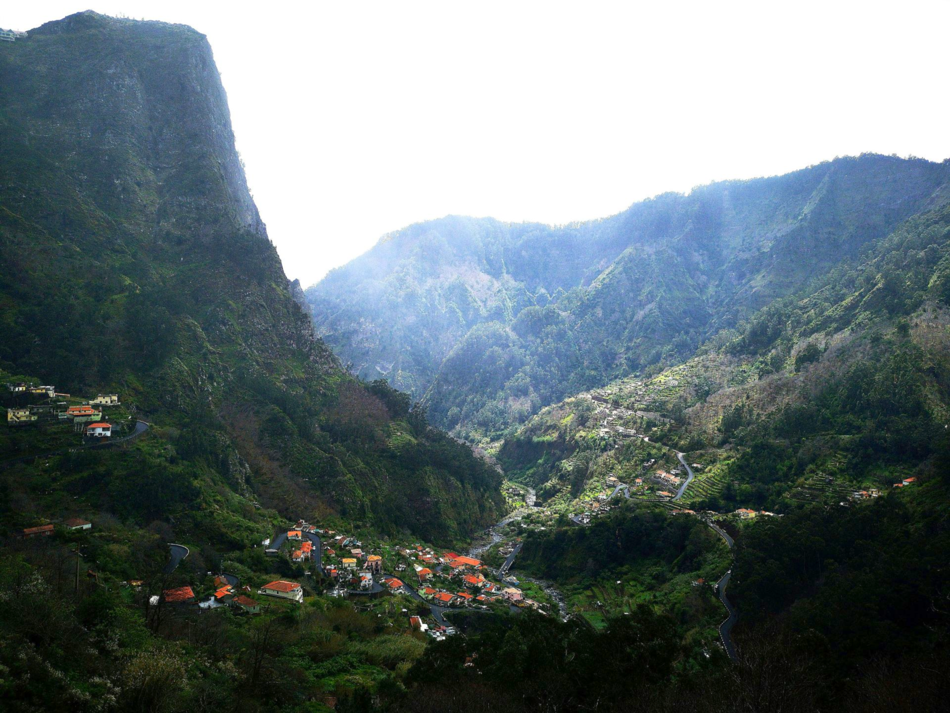 Mountain village nestled in a lush green valley with a view of towering rock formations on the island of Madeira, Portugal.