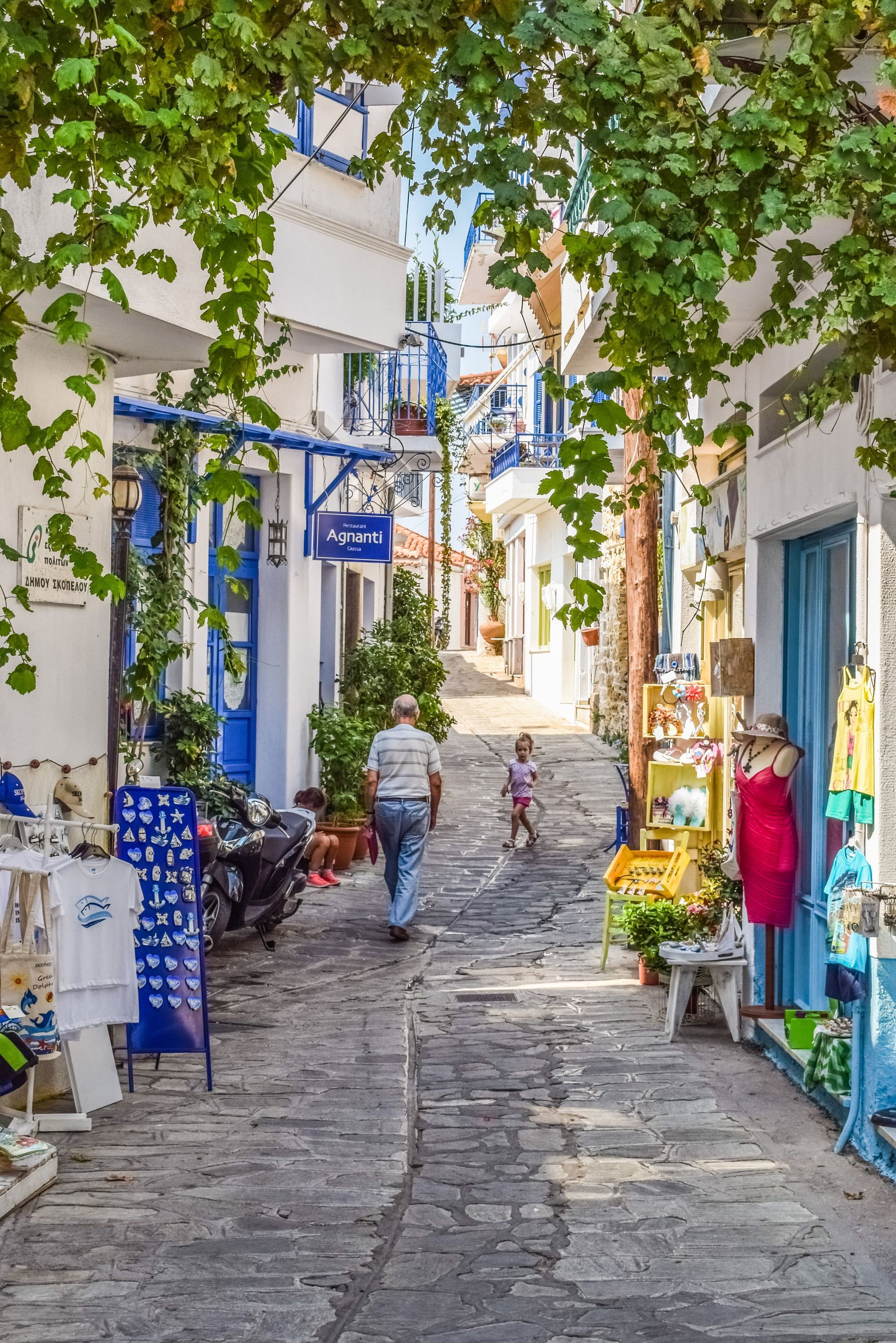 A man and a child are walking down a narrow alleyway between two buildings in Skopelos, Greece.