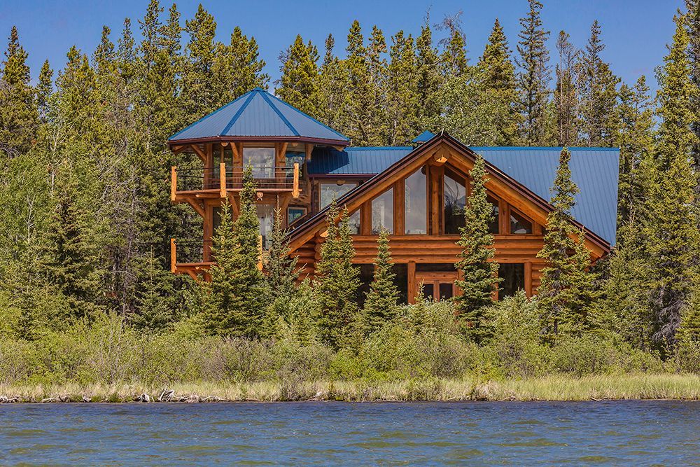 A large log cabin sits on the shore of Chilko Lake, Canada surrounded by trees.