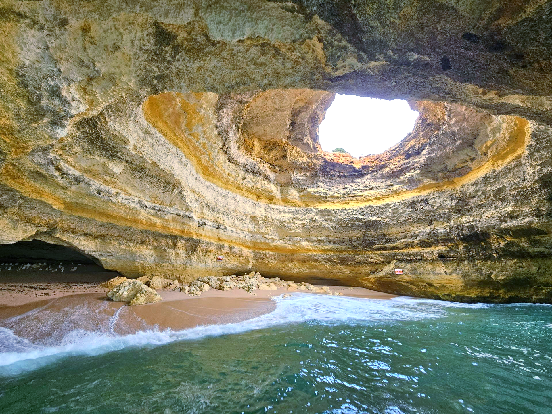 Inside the Benagil Cave with a sandy beach and a large opening to the sky in The Algarve, Portugal.