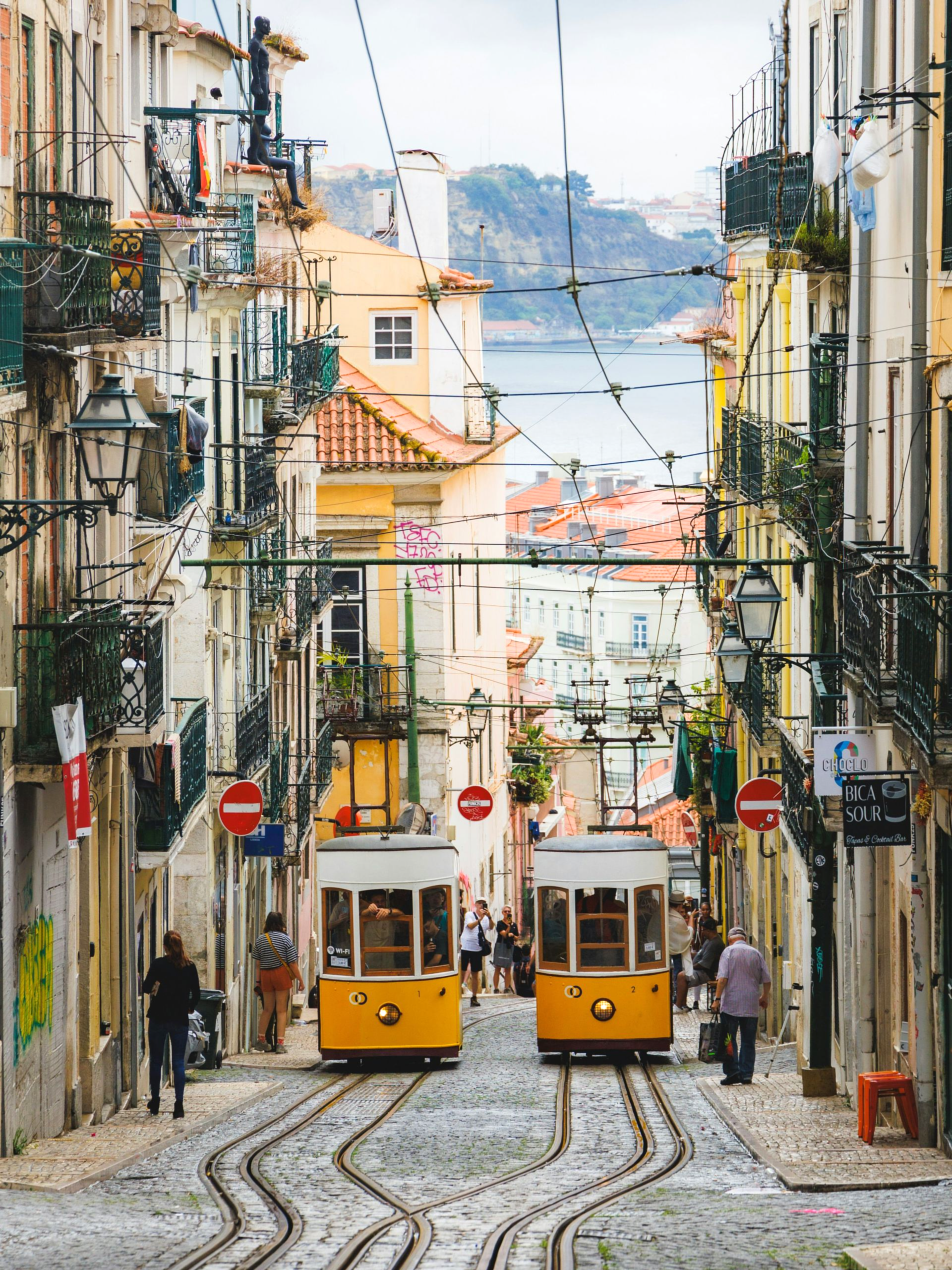 Two yellow trams on cobblestone street in Lisbon, Portugal, passing buildings.