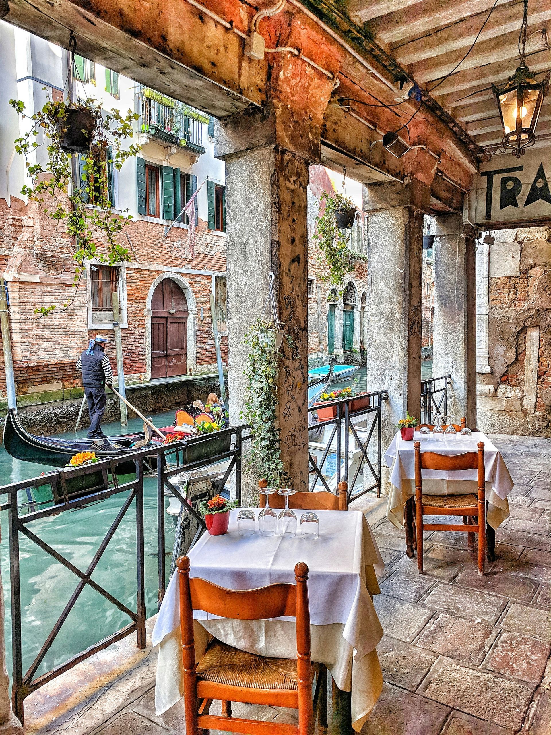 A restaurant with tables and chairs and a gondola in the background in Venice.