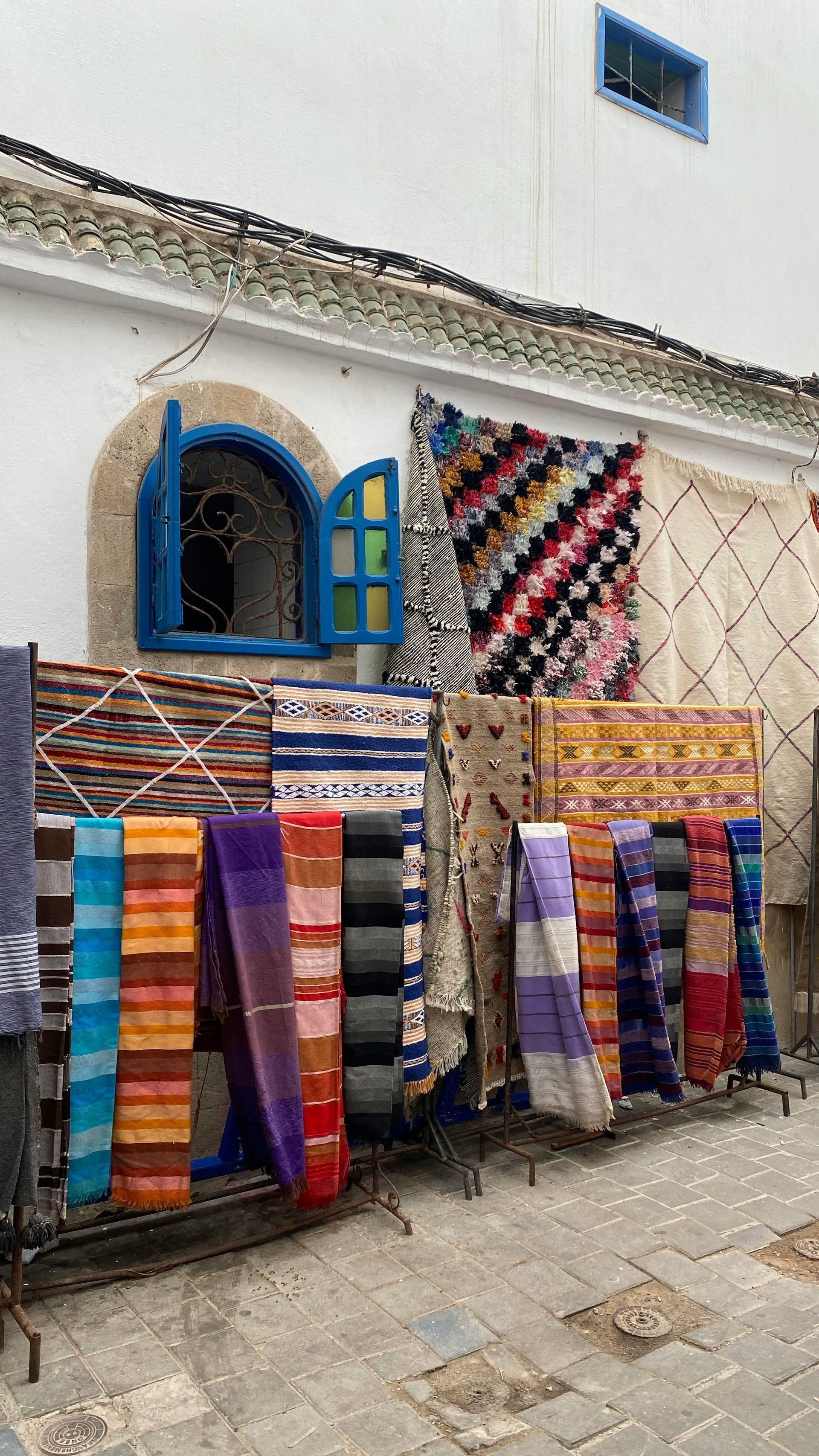 A bunch of colorful rugs are hanging on racks outside of a building in Essaouira, Morocco.