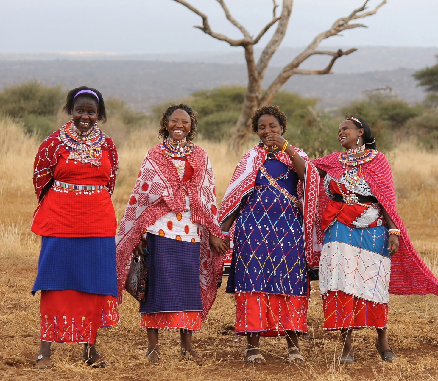 Four Maasai women in colorful traditional clothing, smiling in Amboseli National Park, Kenya.