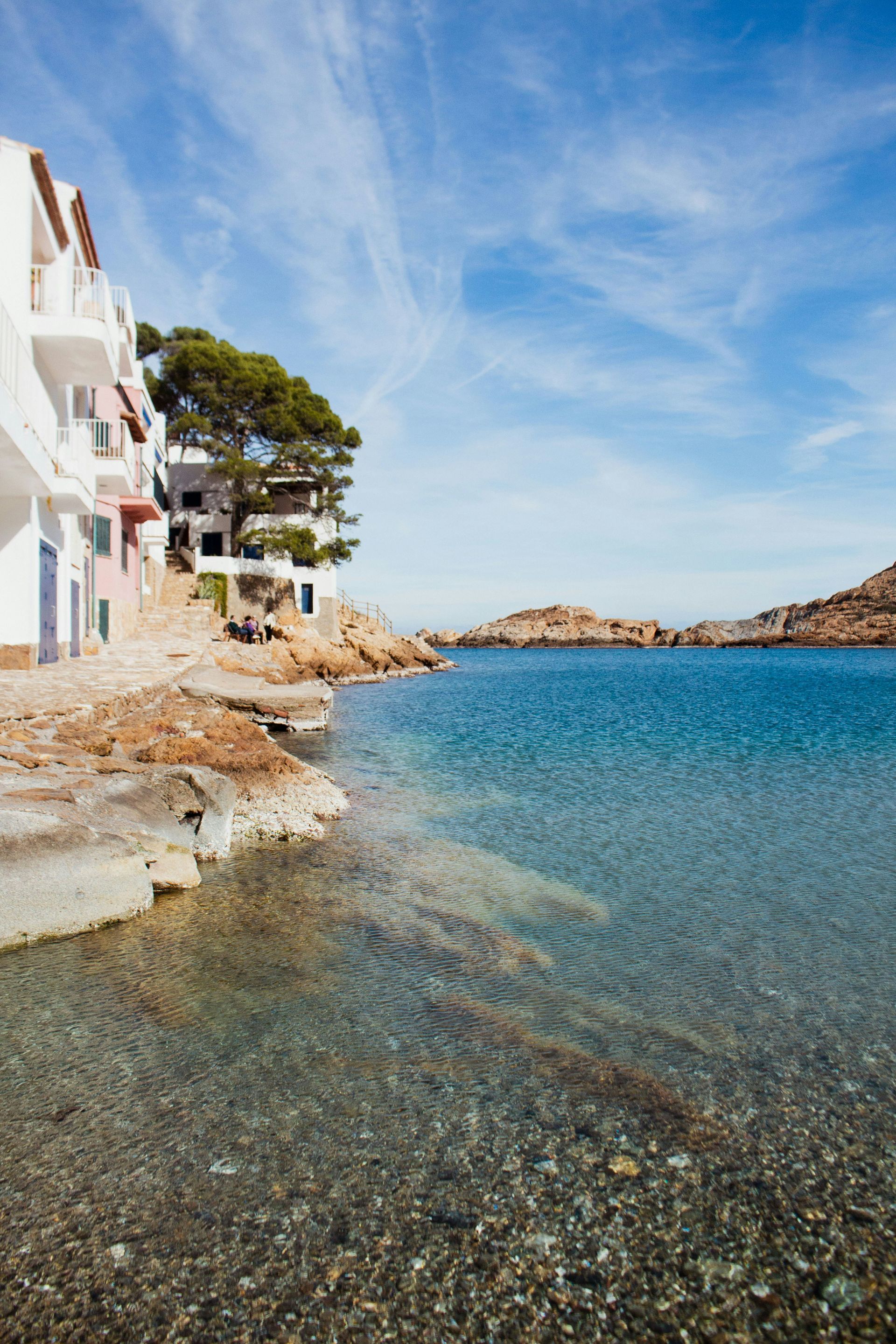 A cliff overlooking a body of water with a house in the background in Begur, Spain.