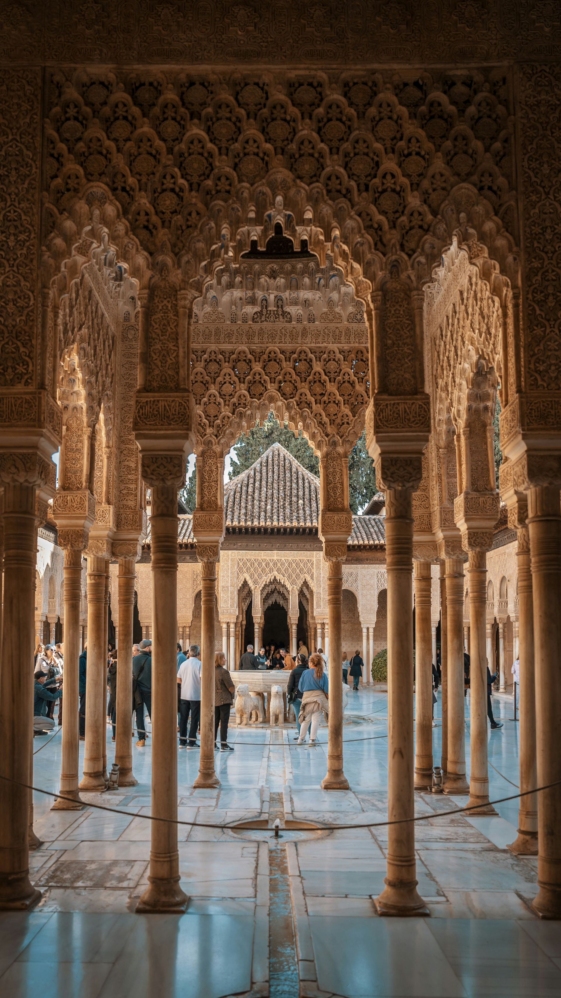 Ornate arches and columns in a courtyard, with visitors in the background, Alhambra, Spain.