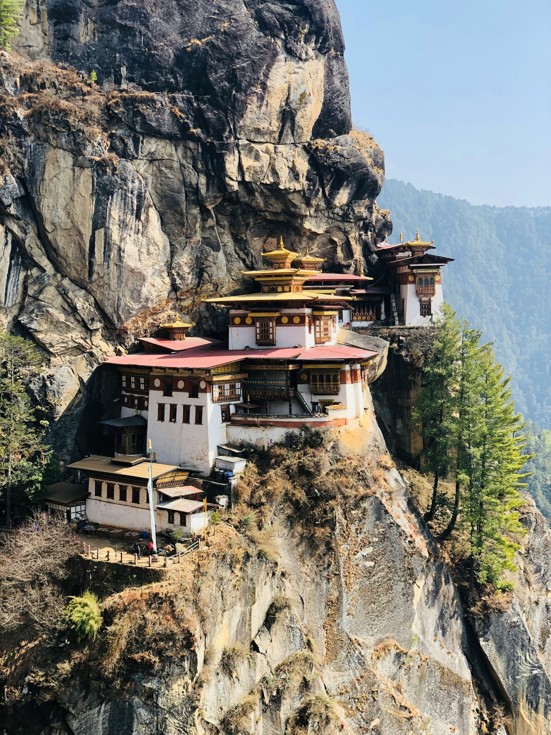 Paro Taktsang, Bhutan, perched on a cliffside with white and gold structures, red roofs, and surrounding mountainous terrain.