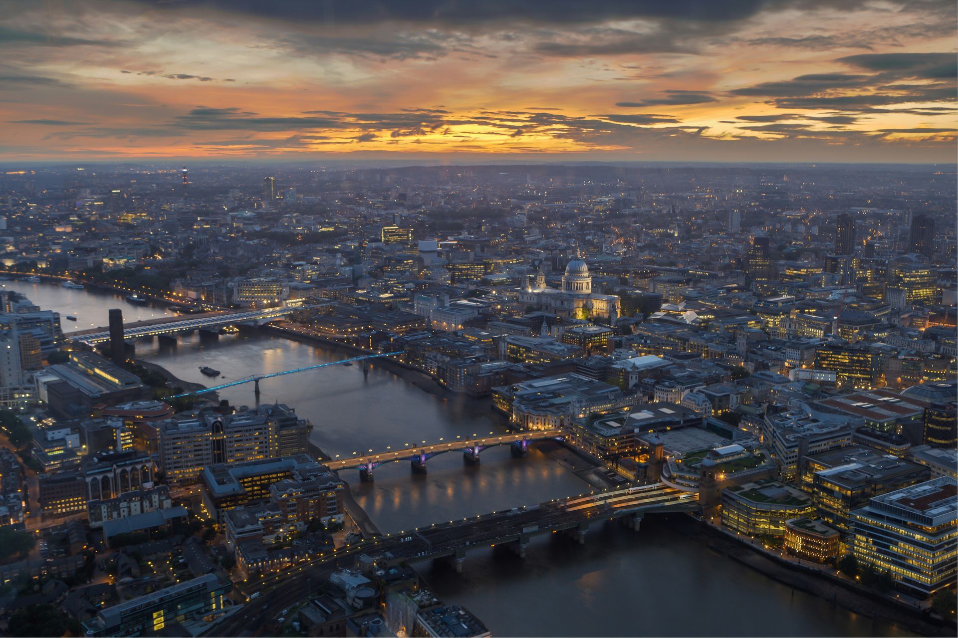 London skyline at dusk, lit city with bridges over the Thames, orange and purple sky.
