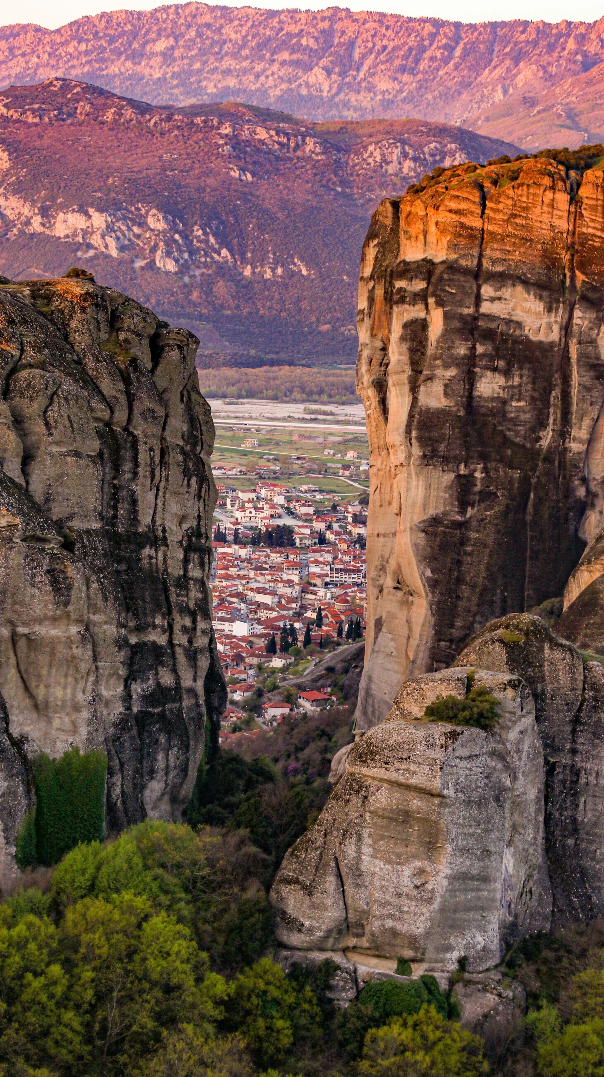 A view of Kalabaka, Greece between two rocky cliffs with mountains in the background.