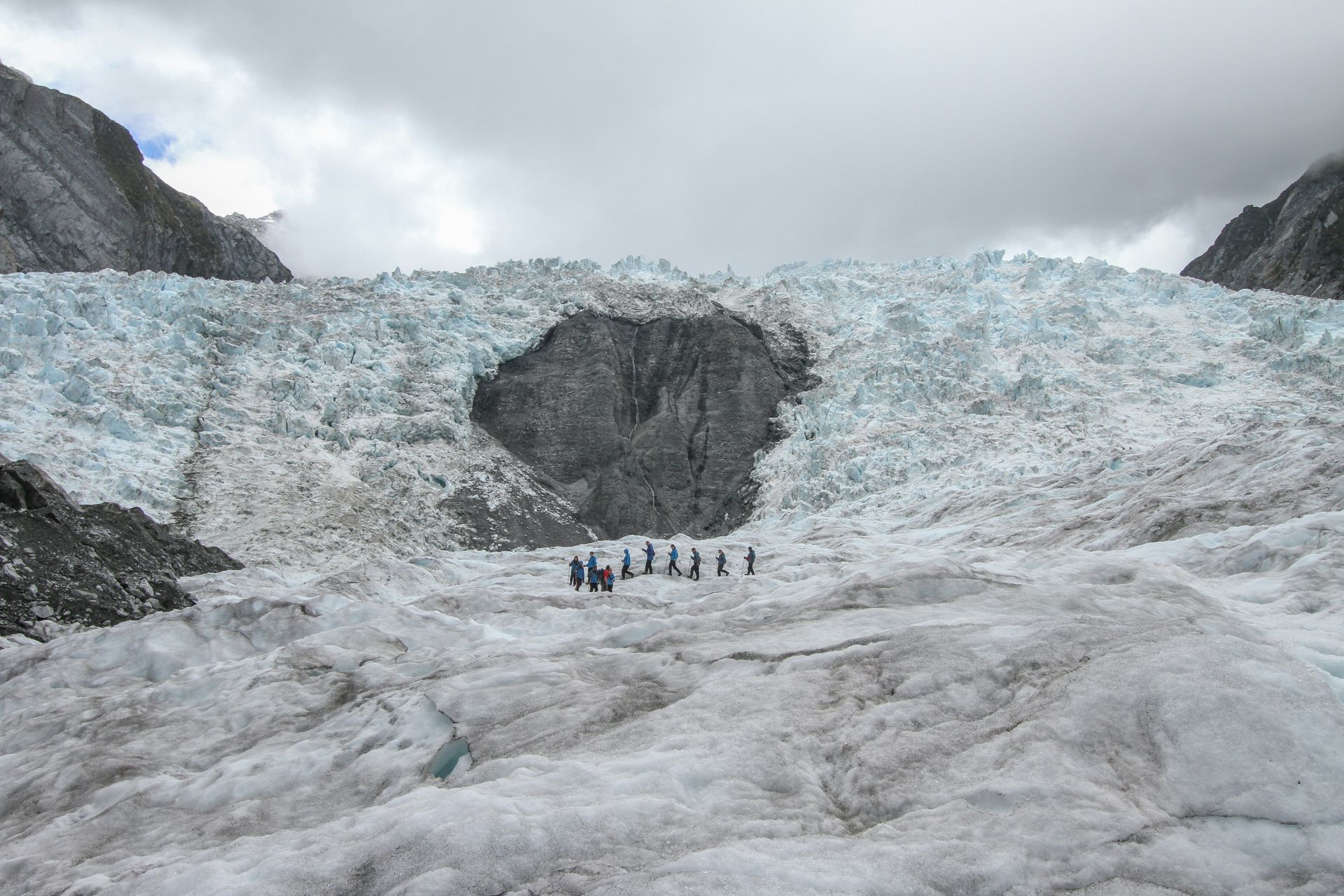 A group of people are hiking across on top of the Franz Josef Glacier in New Zealand.