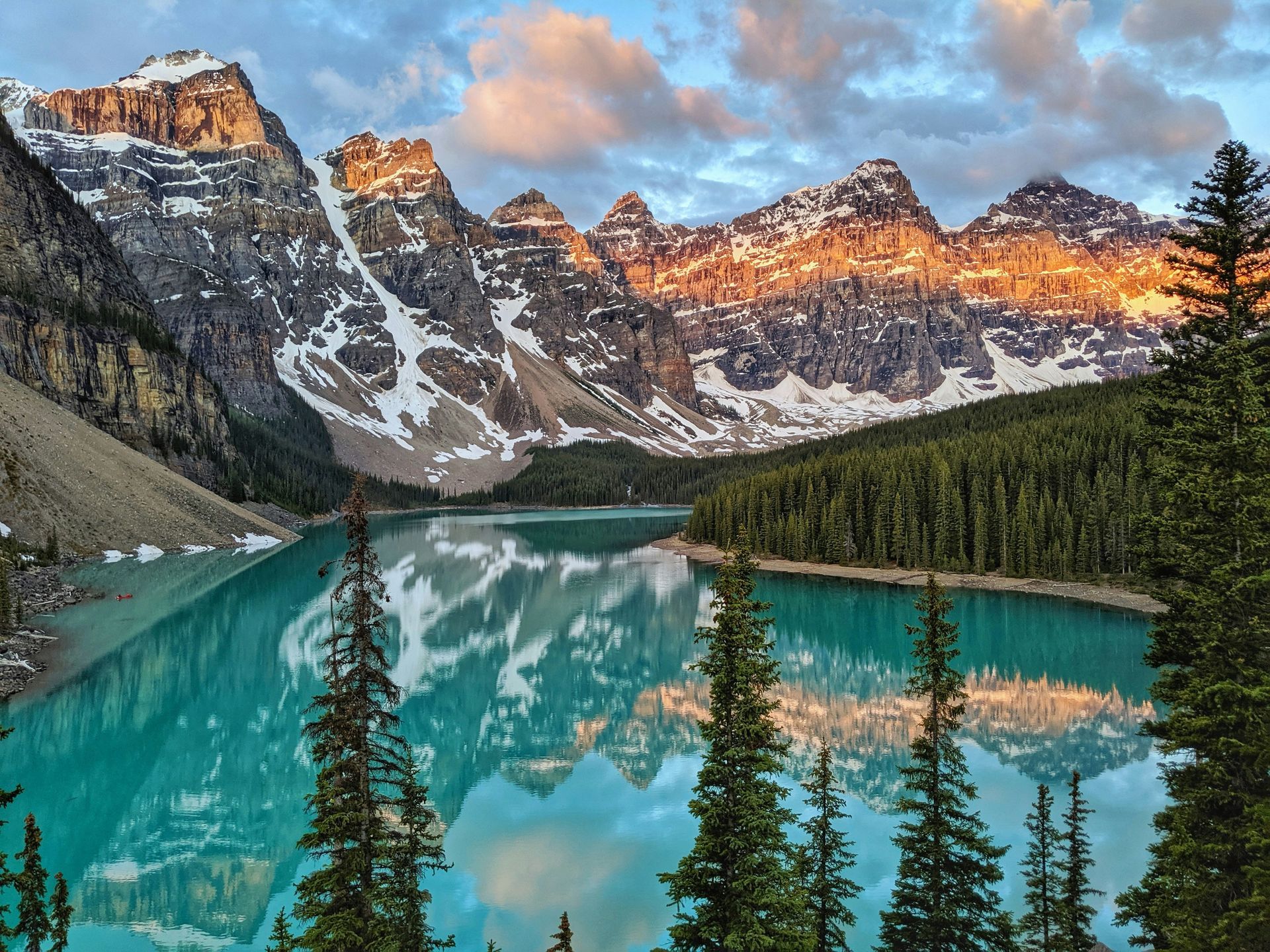 Turquoise Moraine Lake reflects snow-capped mountains lit by golden sunlight framed by evergreen trees in Banff, Canada.