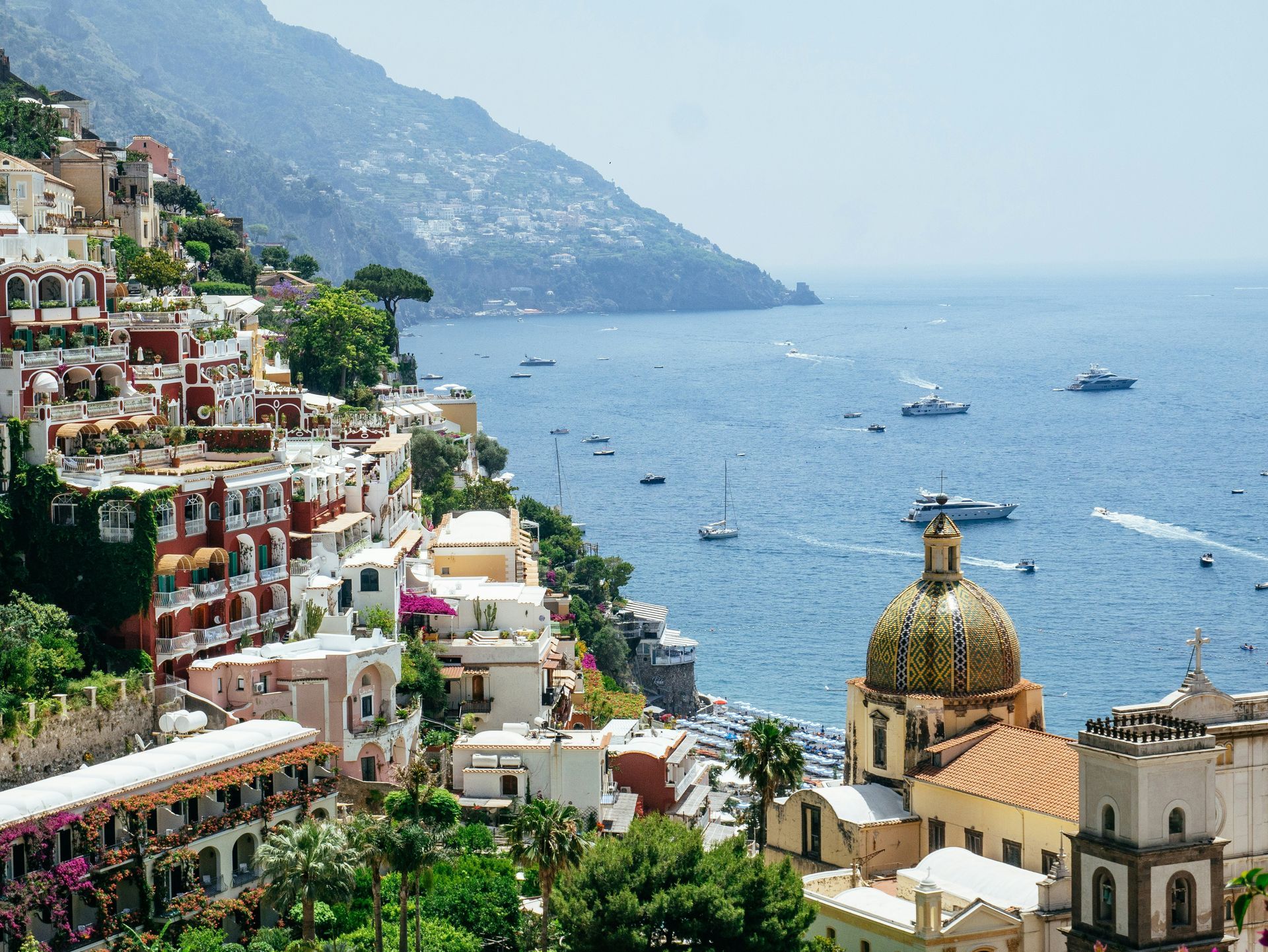 An aerial view of a city overlooking the ocean with boats in the water in the Amalfi Coast.