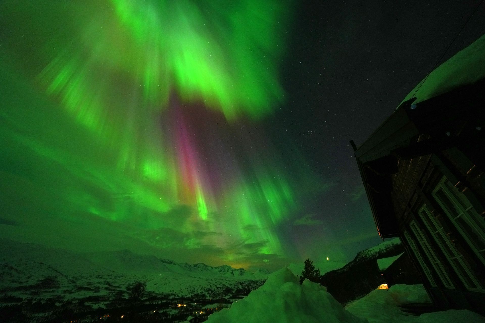 The aurora borealis is shining brightly in the night sky over a snowy landscape in Norway.