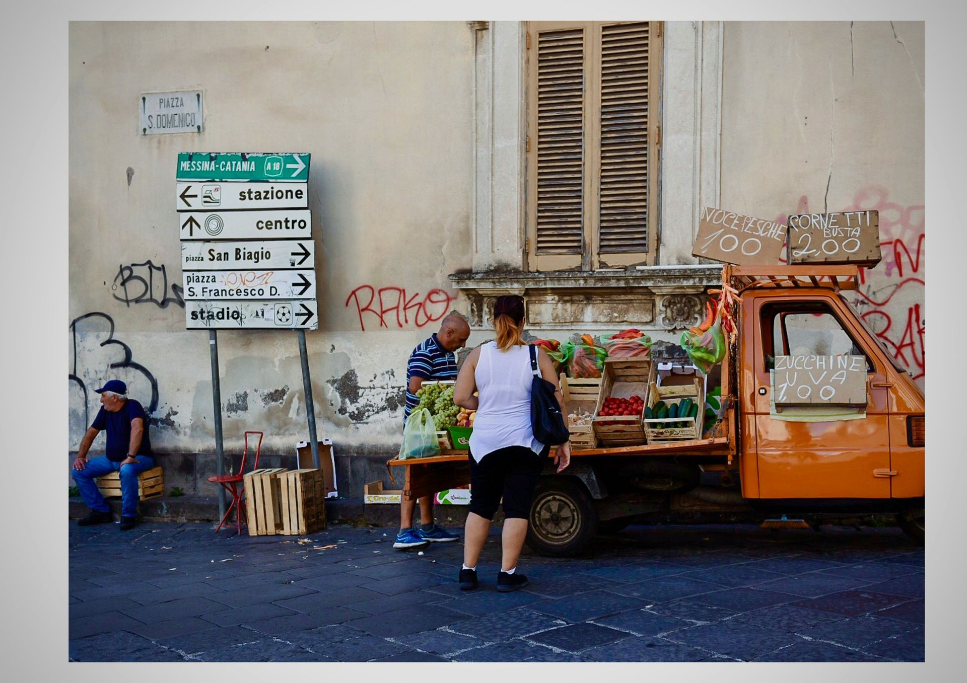 People are buying fruit at a market on the street in Sicily.