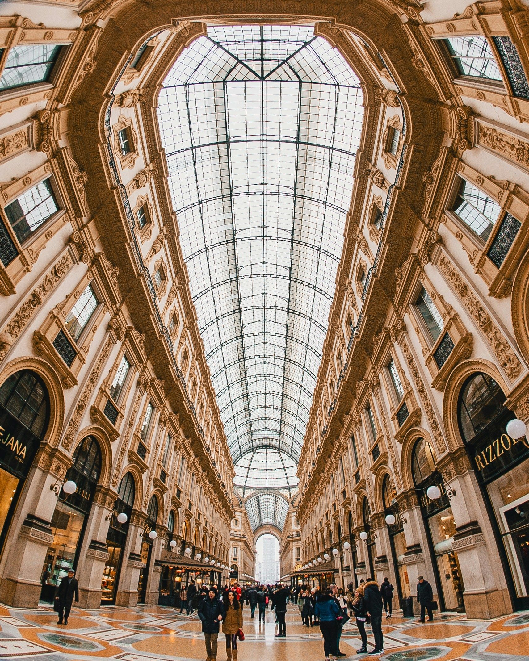 A group of people is walking through the Galleria Vittorio Emanuele II with a glass ceiling in Milan.