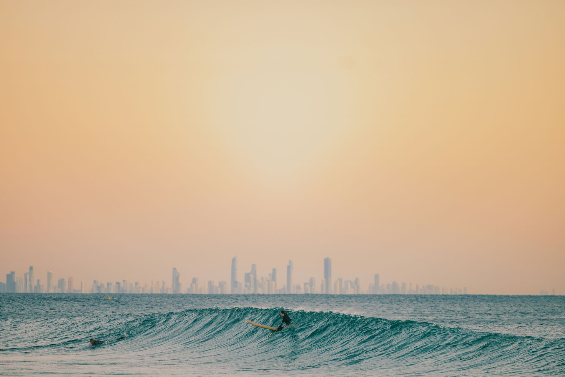 A surfer is riding a wave at Surfers Paradise Beach with Gold Coast city skyline in the background  in Australia. 
