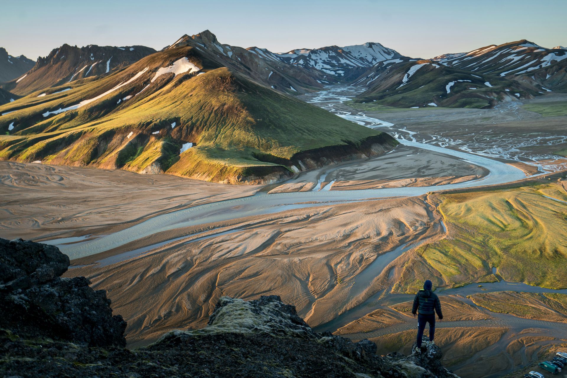 A vast river valley surrounded by green mountains. Sunlight illuminates the landscape in Landmannalaugar, Iceland.