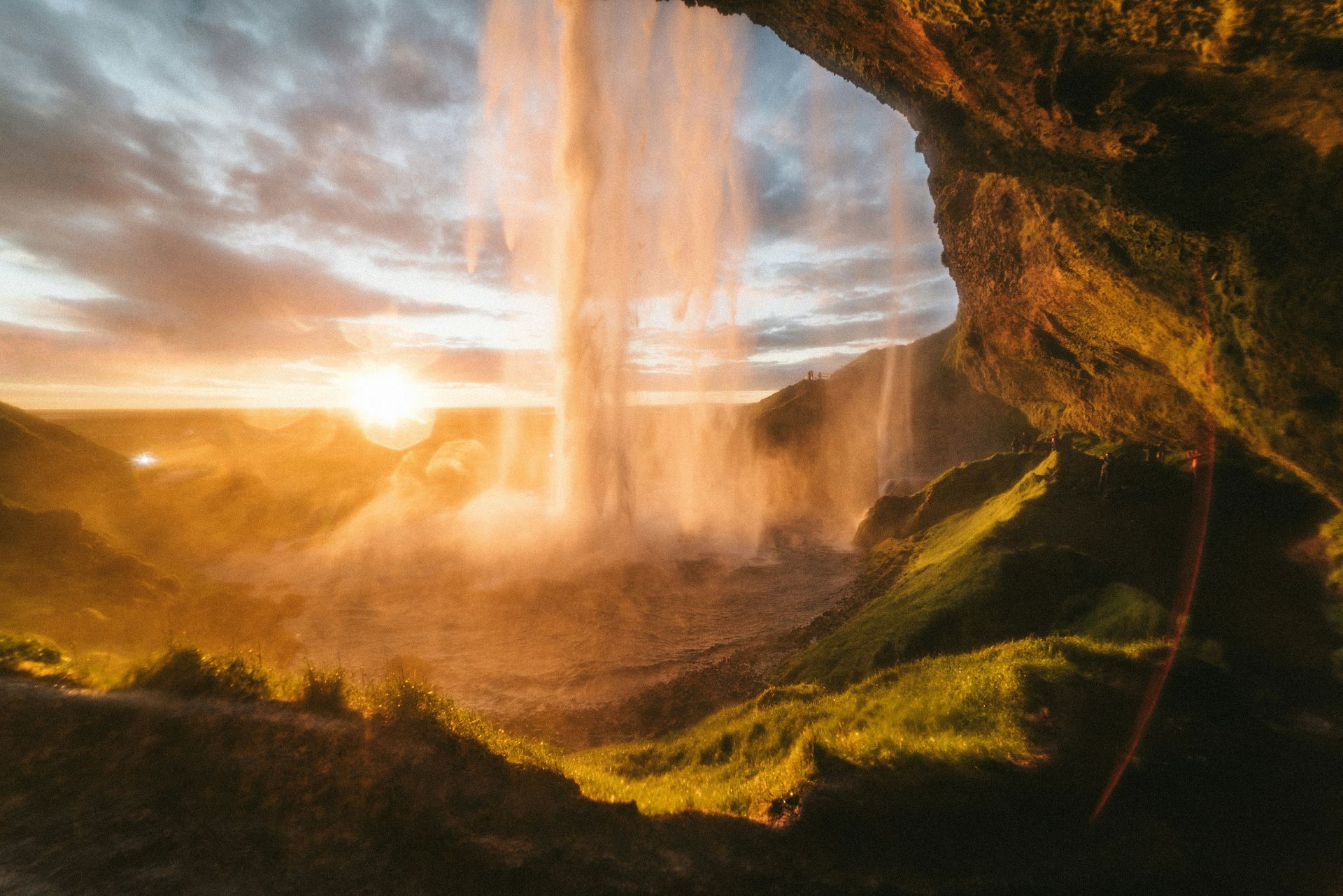 Sunrise illuminates the Seljalandsfoss waterfall from behind, seen from a cave entrance, with mist in Iceland.