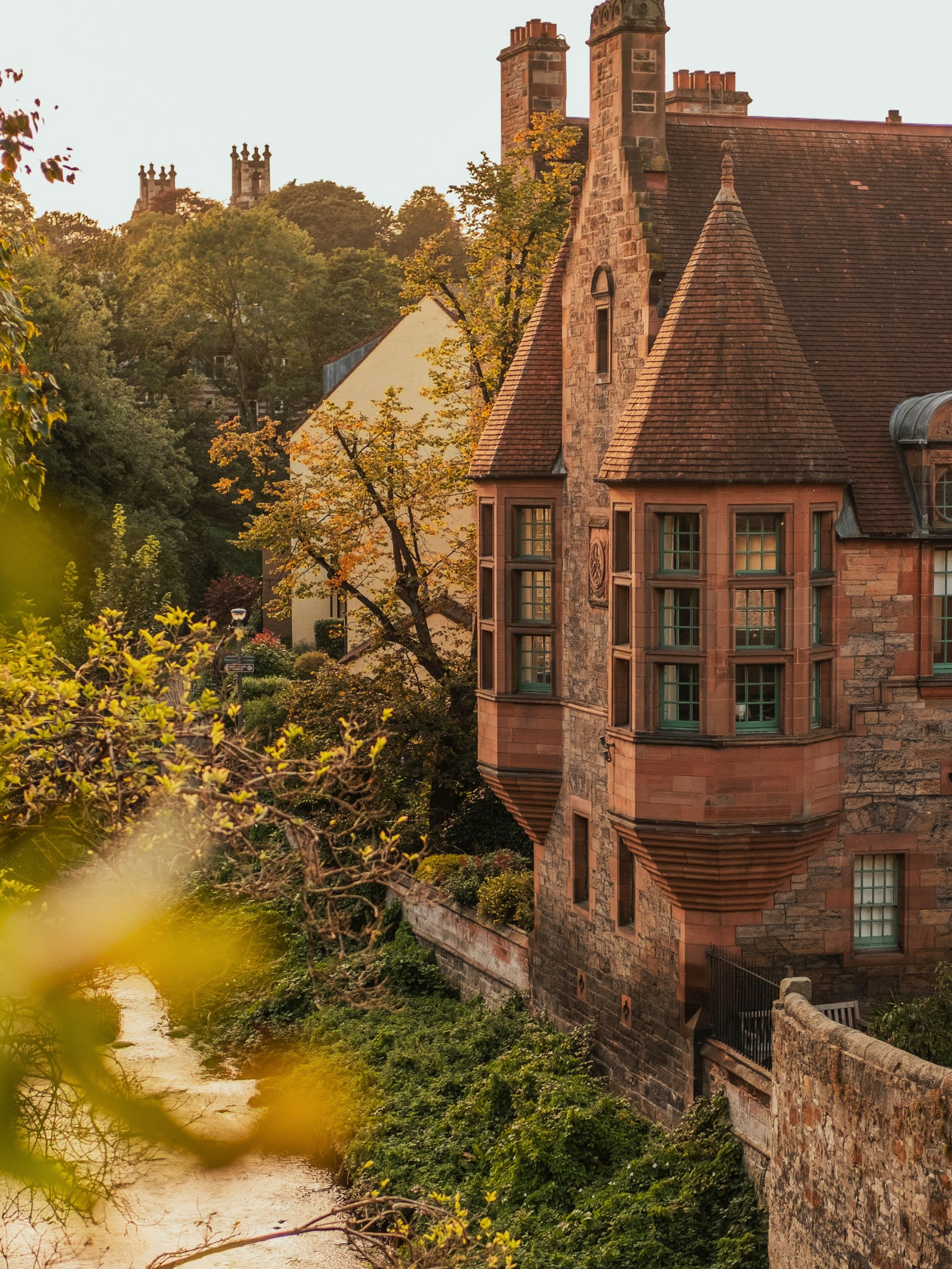 Stone buildings with turrets beside a flowing river under a clear sky in Edinburgh, Scotland.