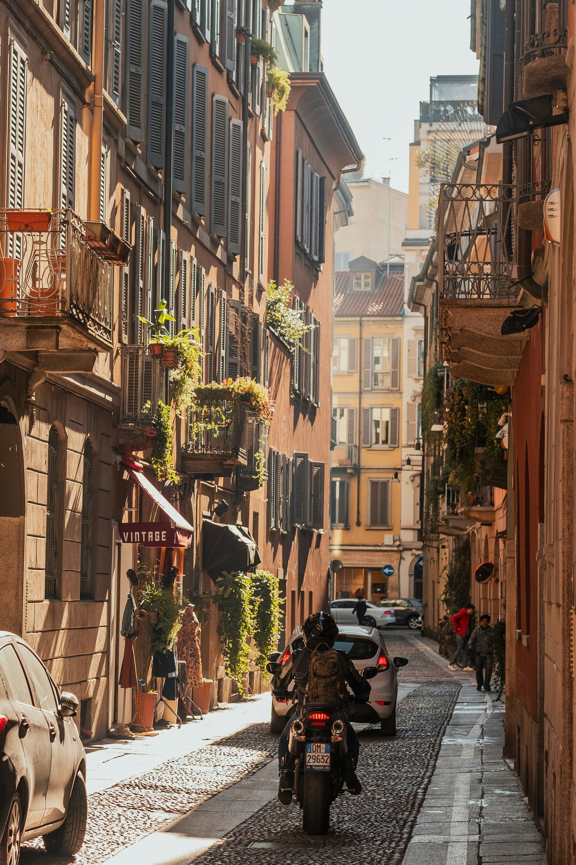 A man is riding a motorcycle down a cobblestone street in Milan.