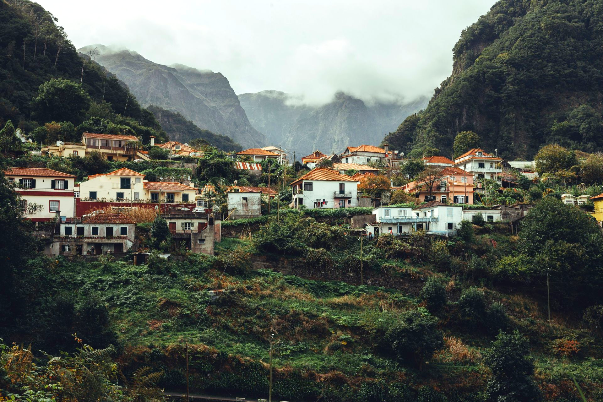 Village nestled in a lush green misty valley, with white houses, red roofs, and mountains on the island of Madeira, Portugal.