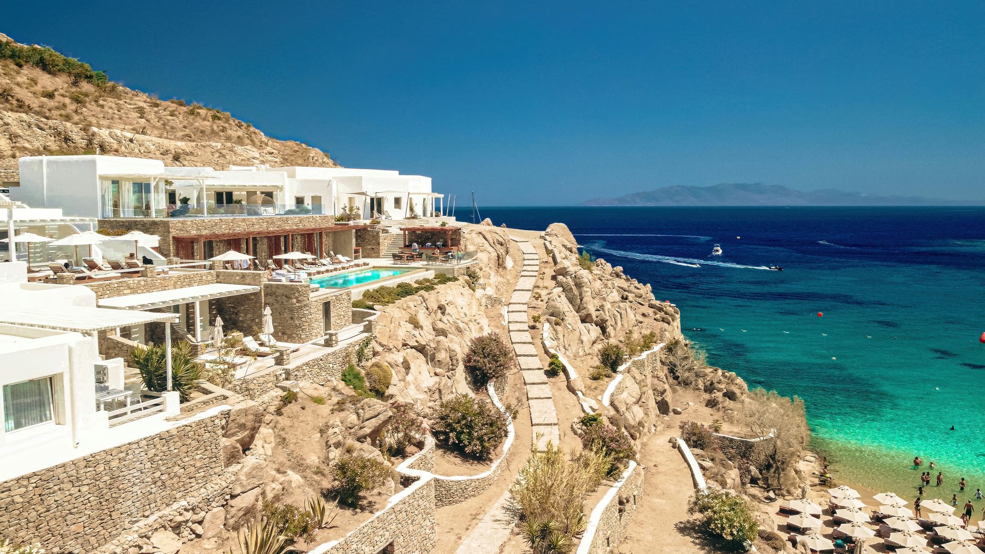 A large white building is sitting on top of a cliff overlooking the ocean in Mykonos, Greece.