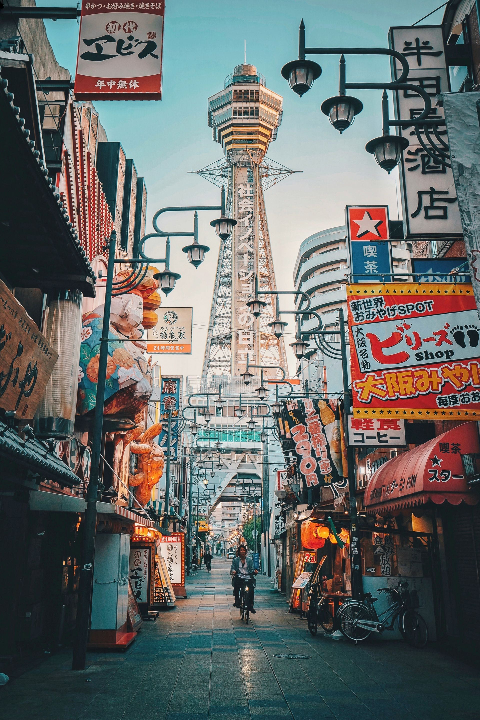 Busy street scene in Japan with Tsutenkaku Tower. Buildings with neon signs line the street, filled with people.