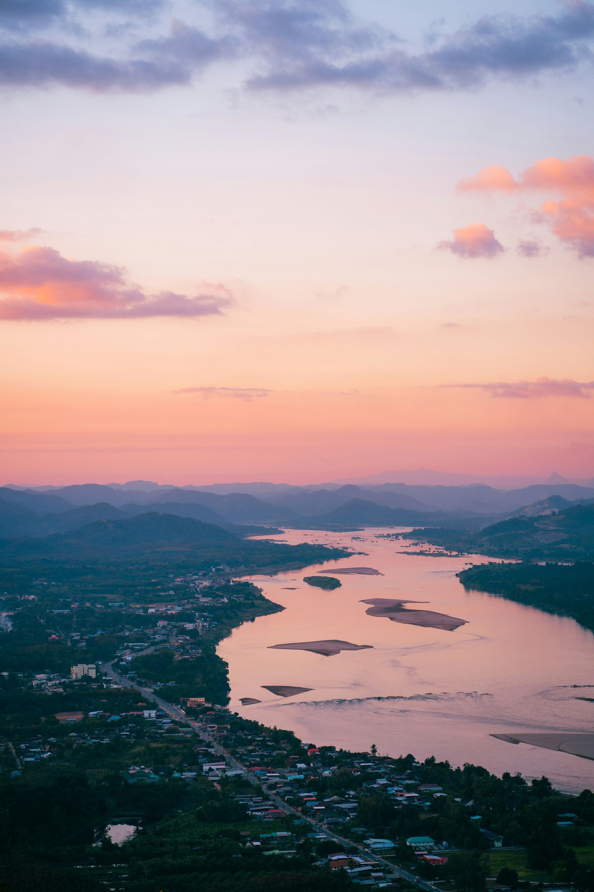 Sunset over the Mekong River, town below, pink and purple sky, green hills.