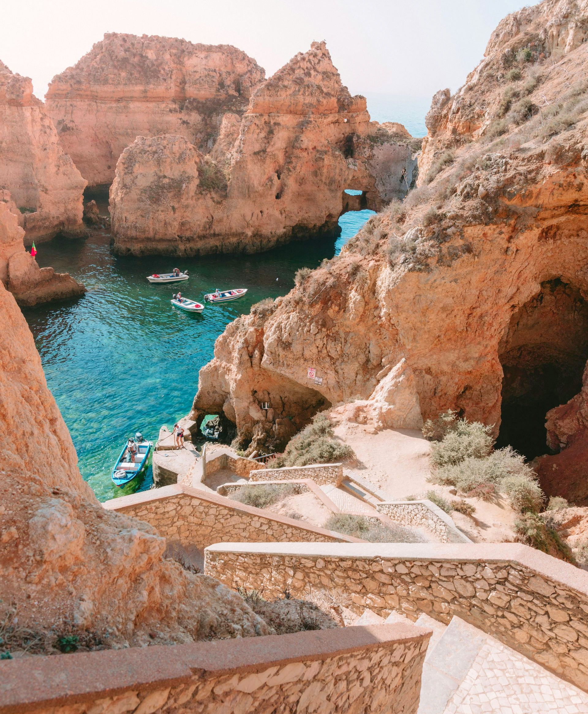 Stone steps leading to a turquoise cove with boats and rock formations in Lagos, Portugal.