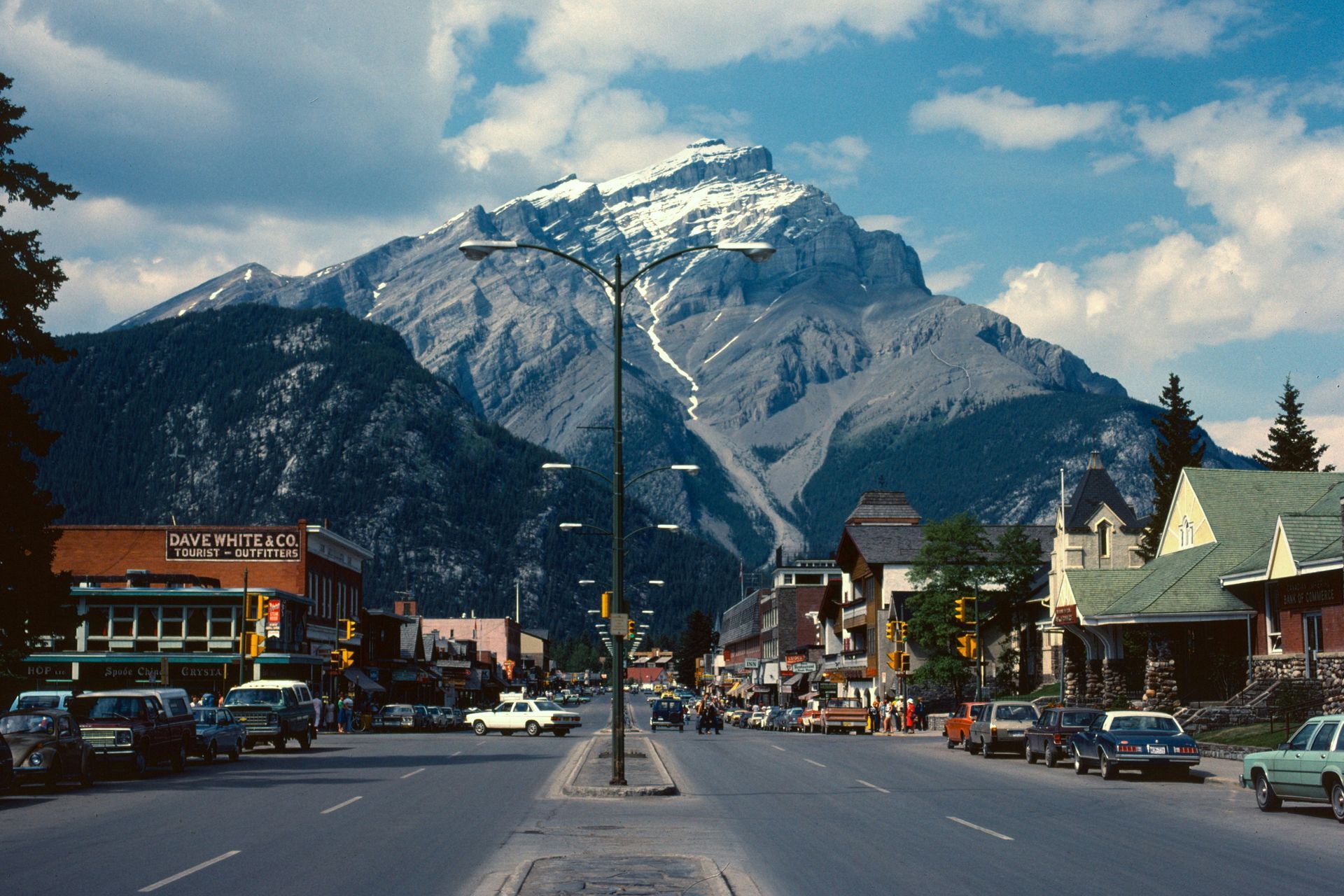 Street in Banff, Canada, with buildings lining the road and a large, snow-capped mountain in the background.