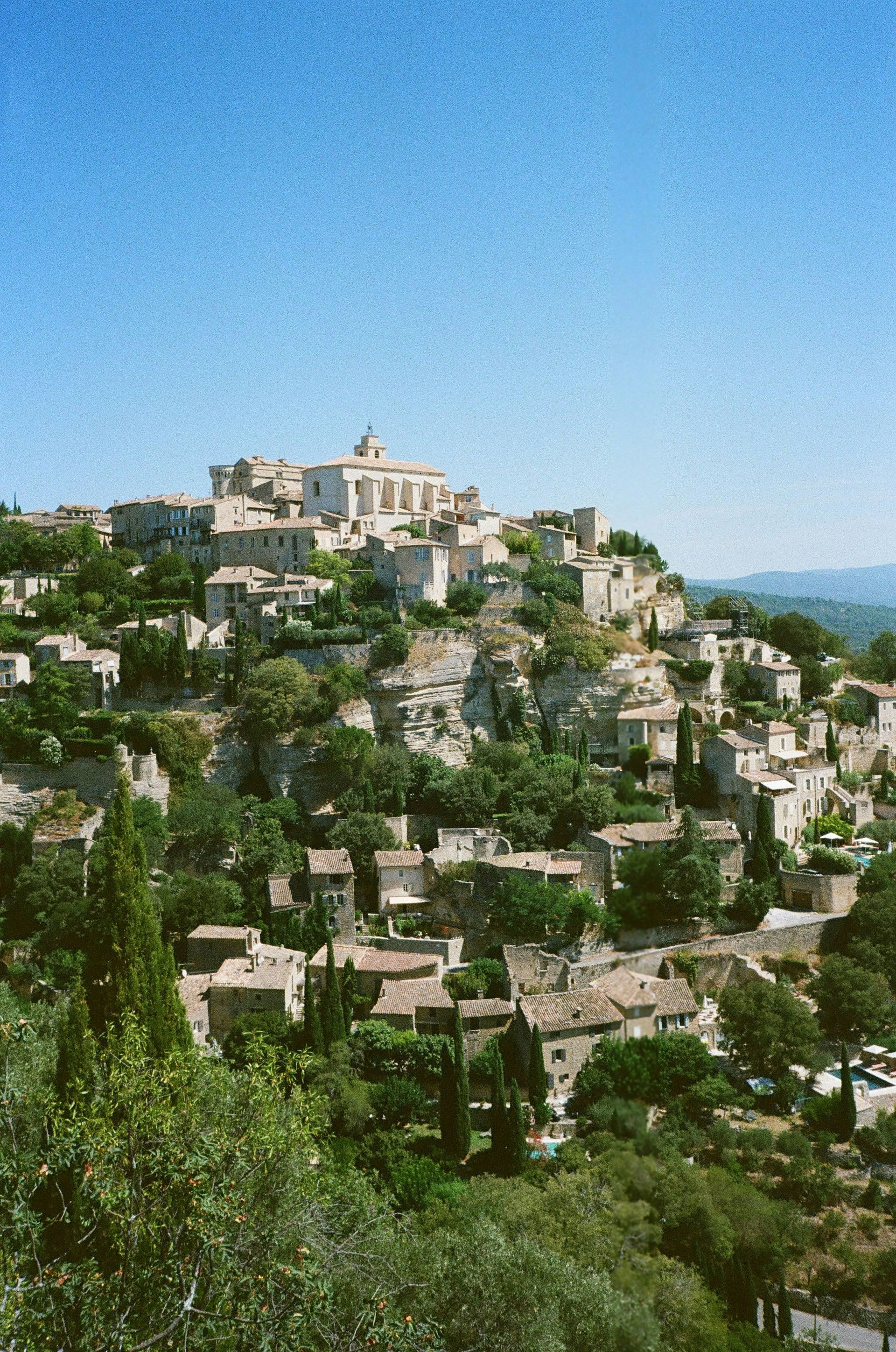 The small town of Gordes sits on top of a hill surrounded by trees in Luberon, France.