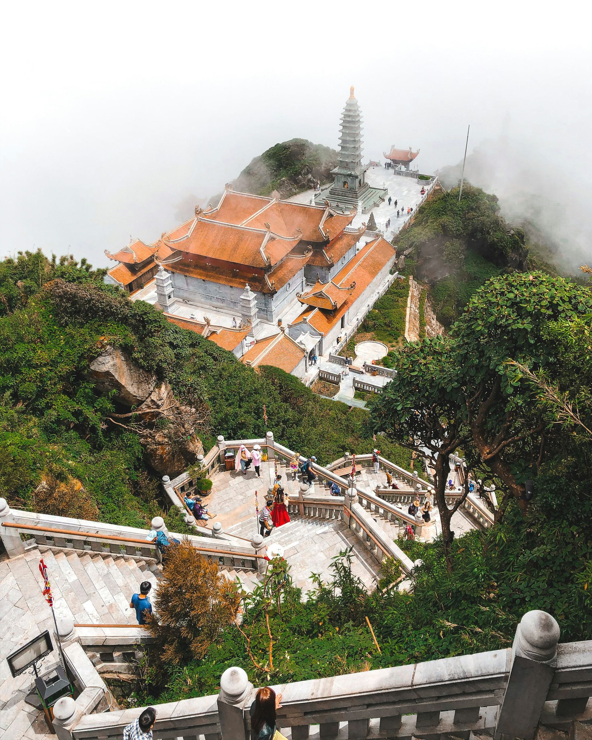 A temple complex atop a lush green mountain in a misty setting in Sapa, Vietnam. 