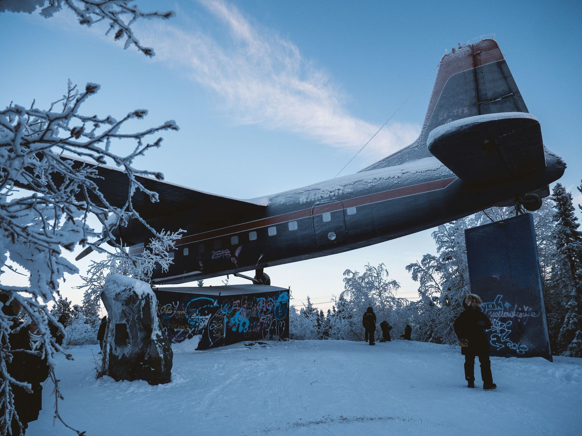 An old airplane monument on a snowy hill. Winter landscape with trees, snow, and some people in Yellowknife, Canada.