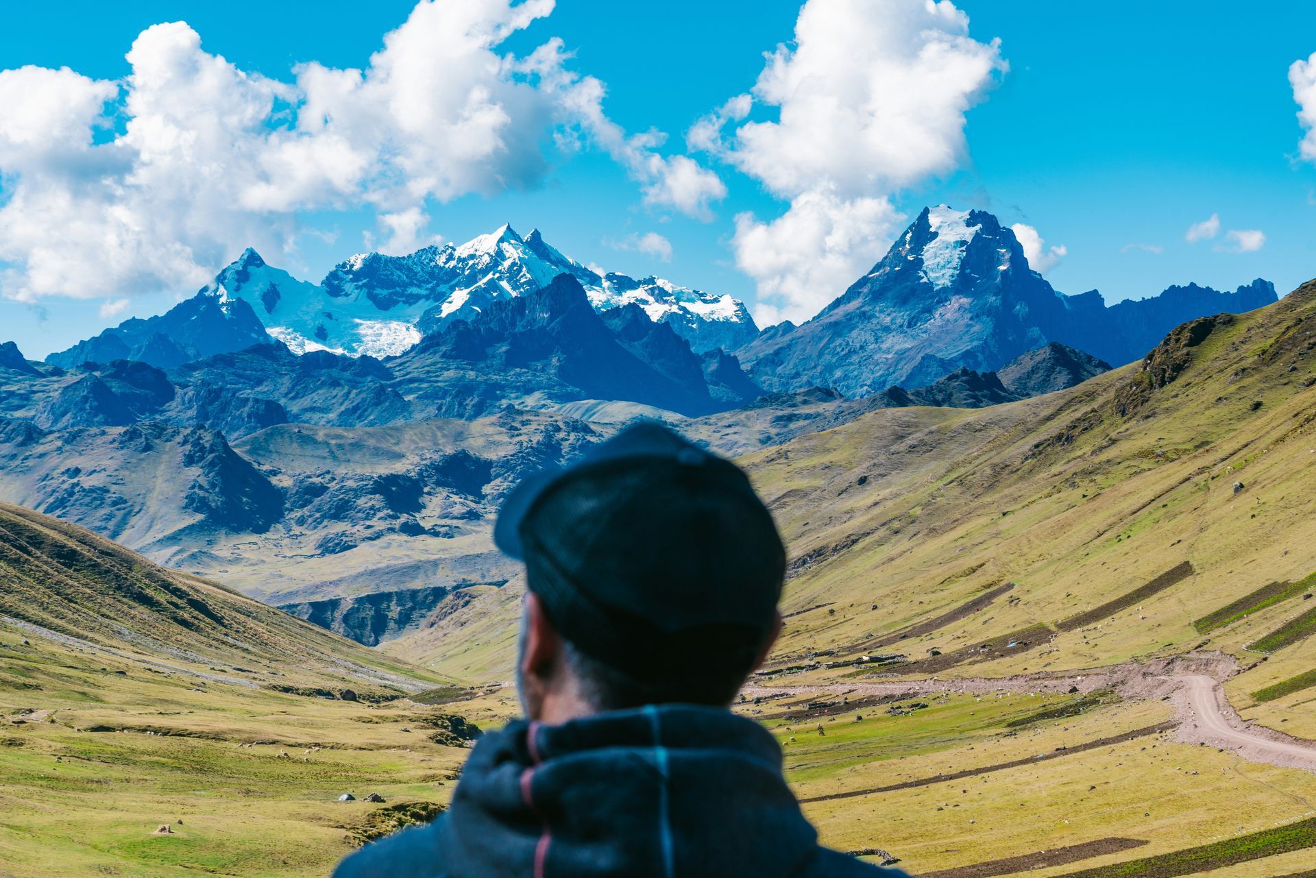 A man is standing in a field looking at a mountain range in the Sacred Valley of Peru.