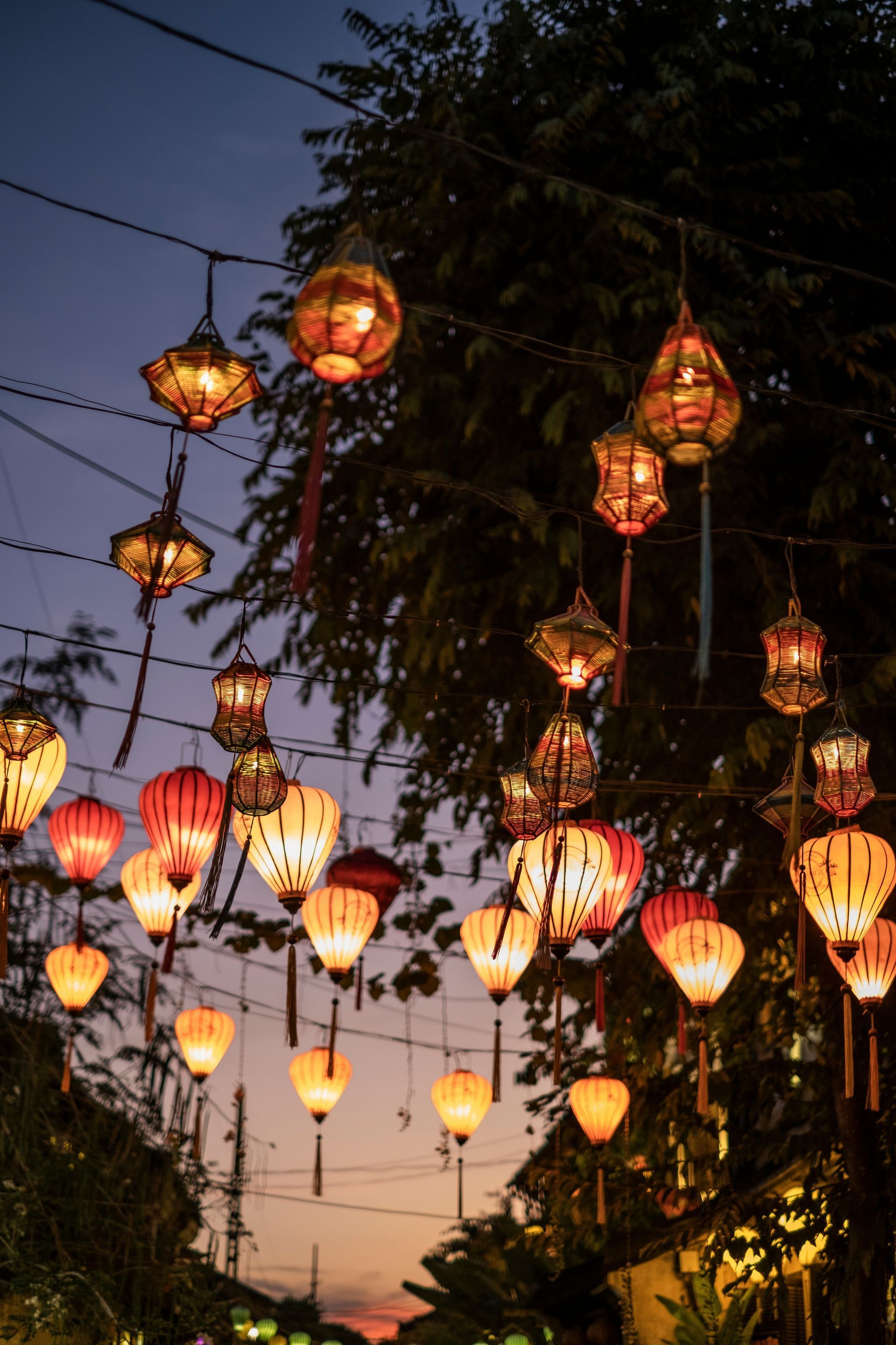 Evening street scene with colorful, illuminated lanterns hanging overhead in Hội An, Vietnam.