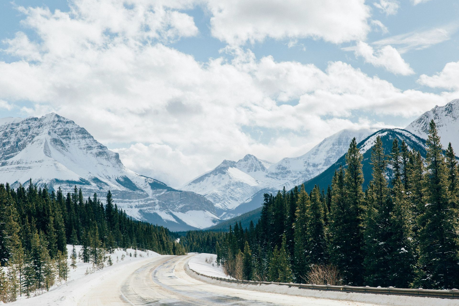 A snowy road with mountains in the background and trees on the side in Canada.