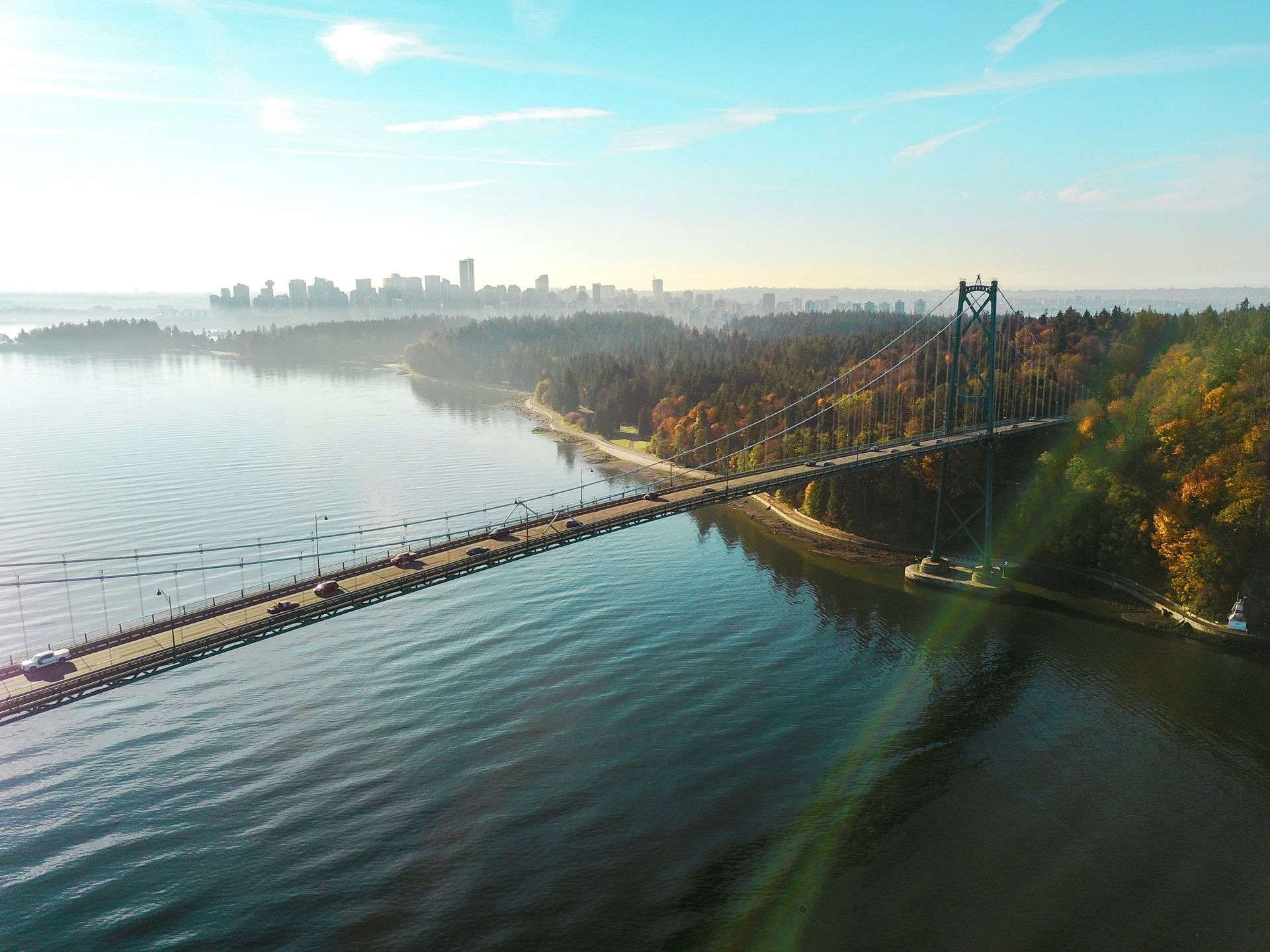 Lions Gate Bridge in Vancouver, BC, spanning a body of water with city skyline in the background on a sunny day.