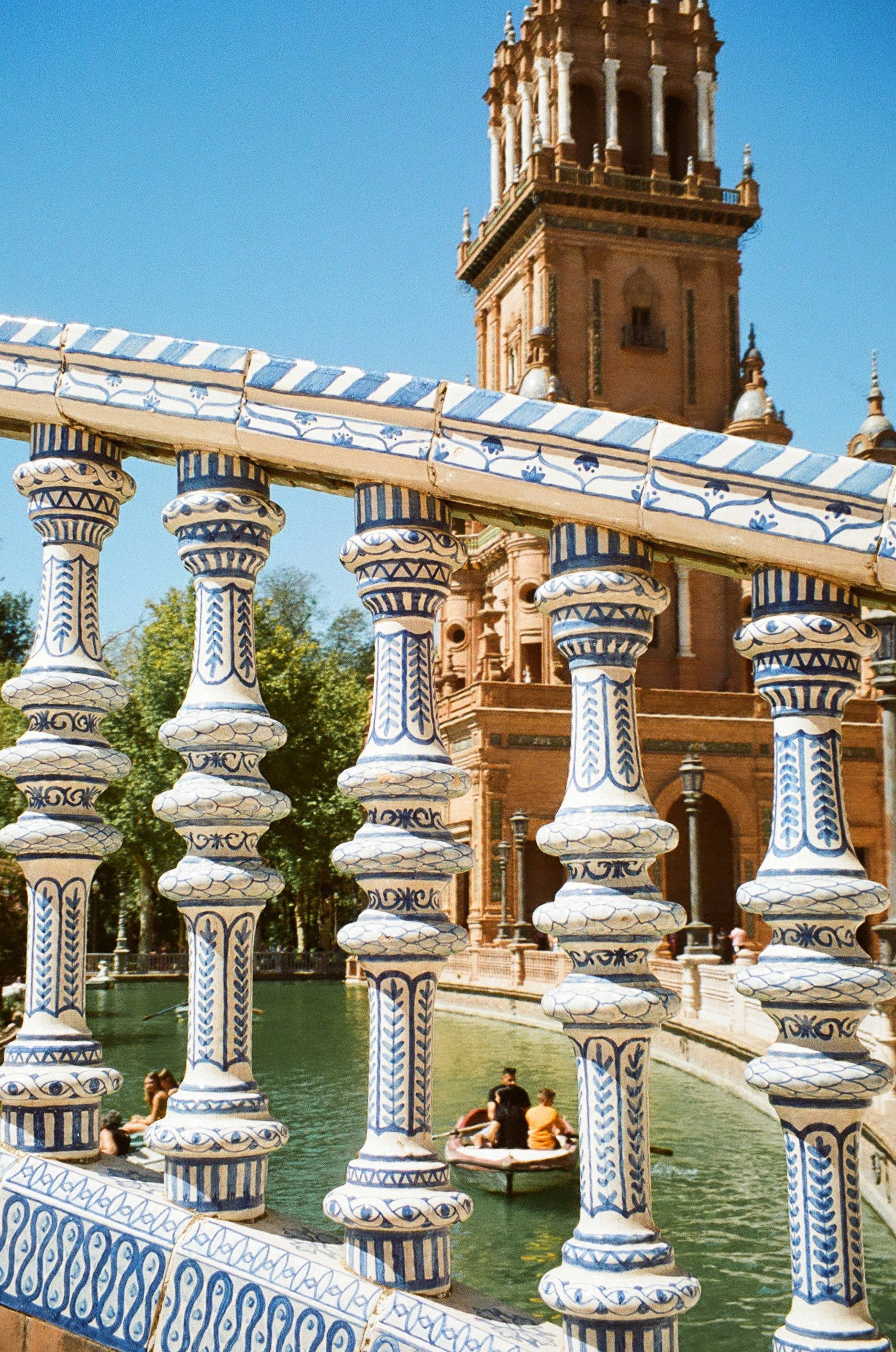 Balustrade with blue and white tile, overlooking a canal with a boat. A brick tower in the background in Sevilla, Spain.