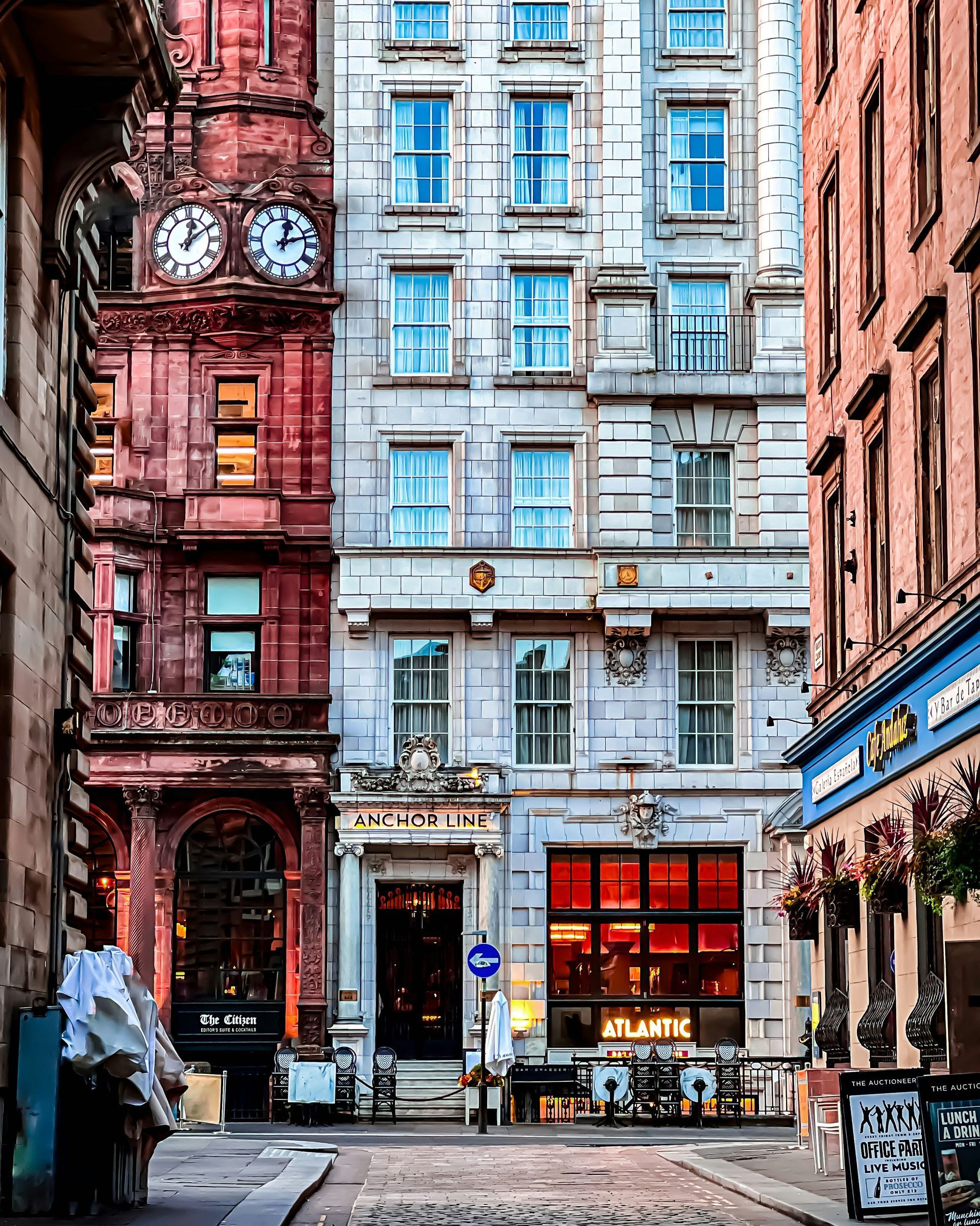 Narrow city street with diverse stone buildings, including a pub and clock tower in Glasgow, Scotland.