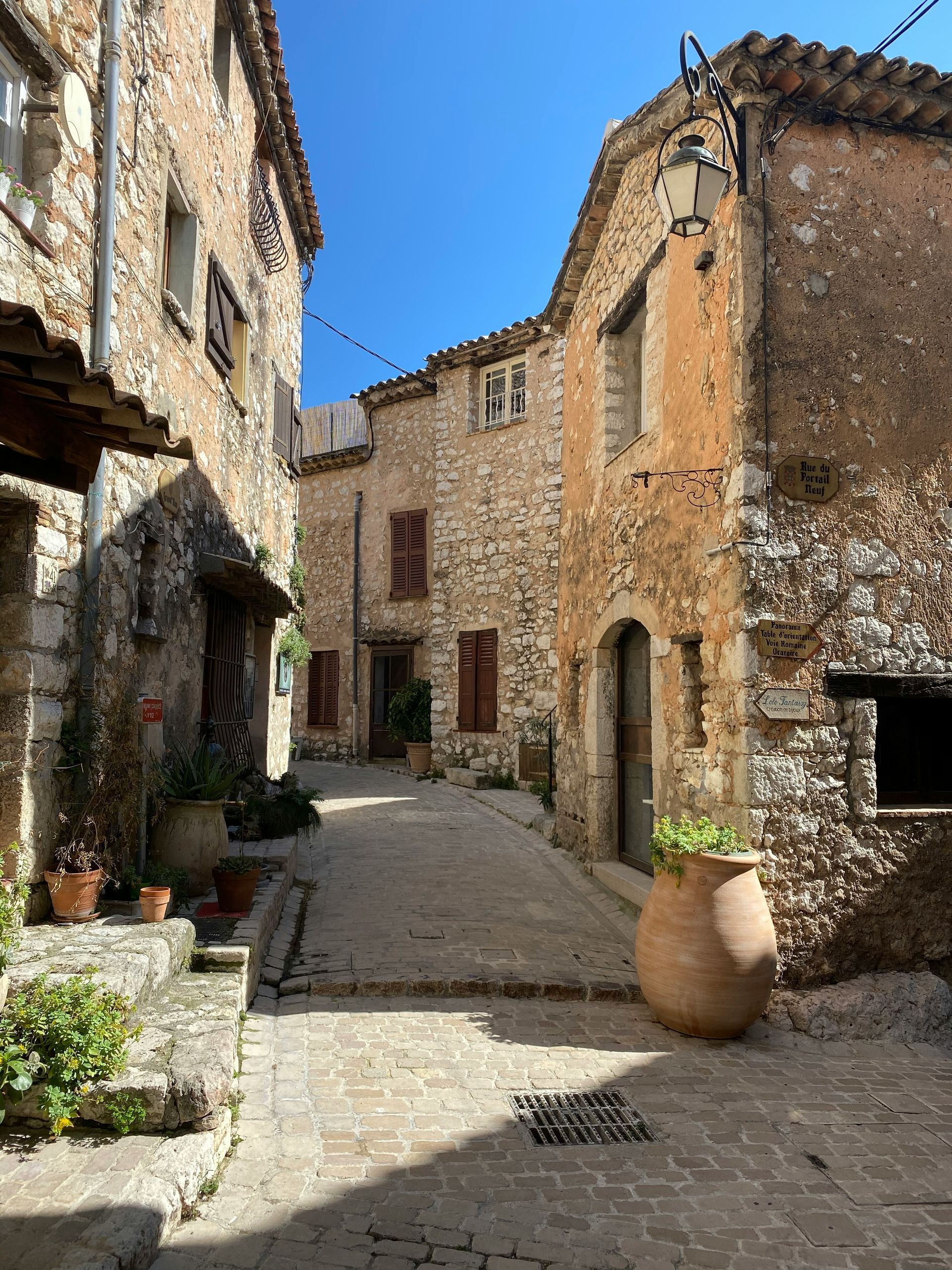 A narrow alleyway between two stone buildings with potted plants on the sidewalk in the Côte d'Azur.