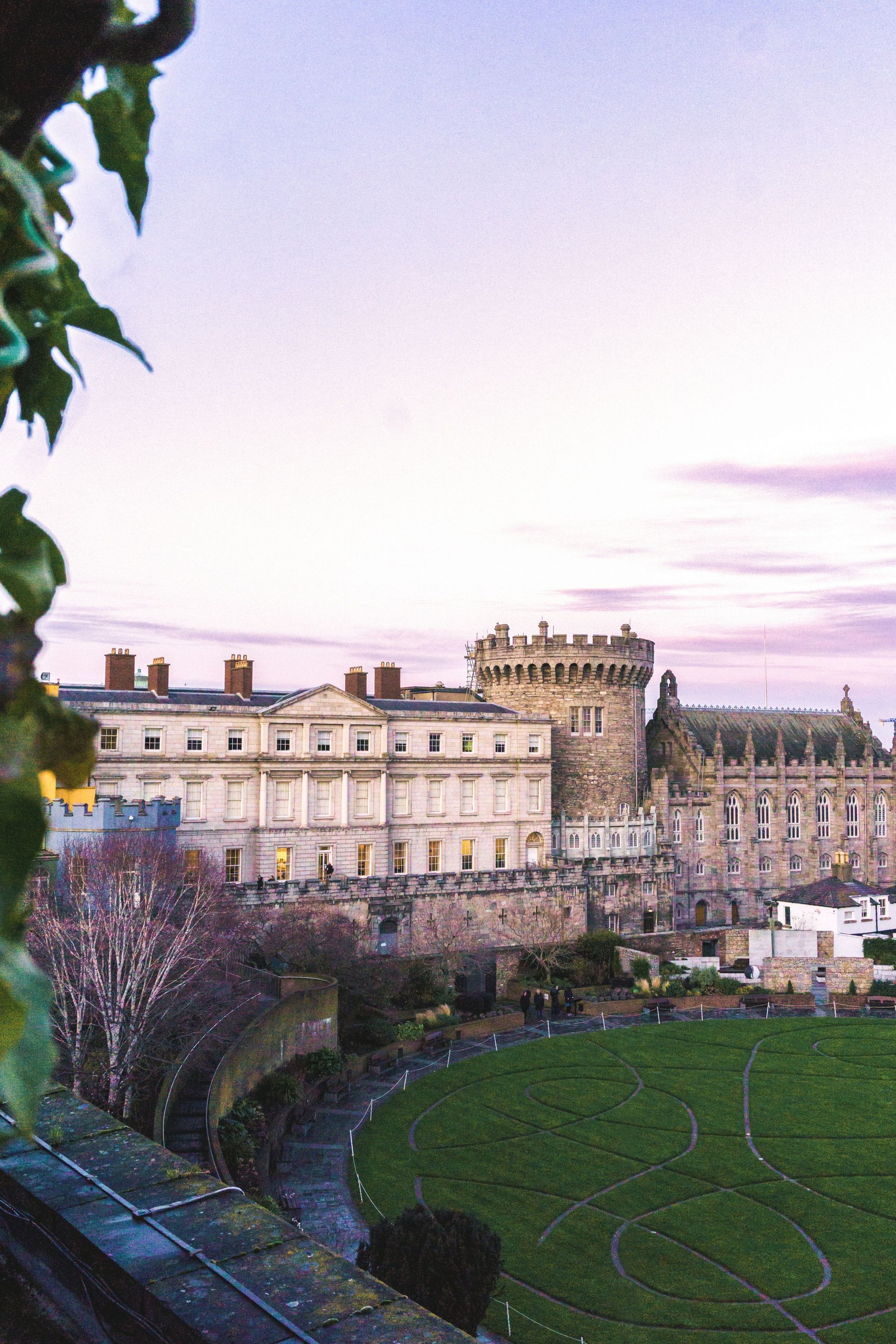 Dublin Castle, Ireland, under a twilight sky; buildings with stone tower and green lawn in the foreground.