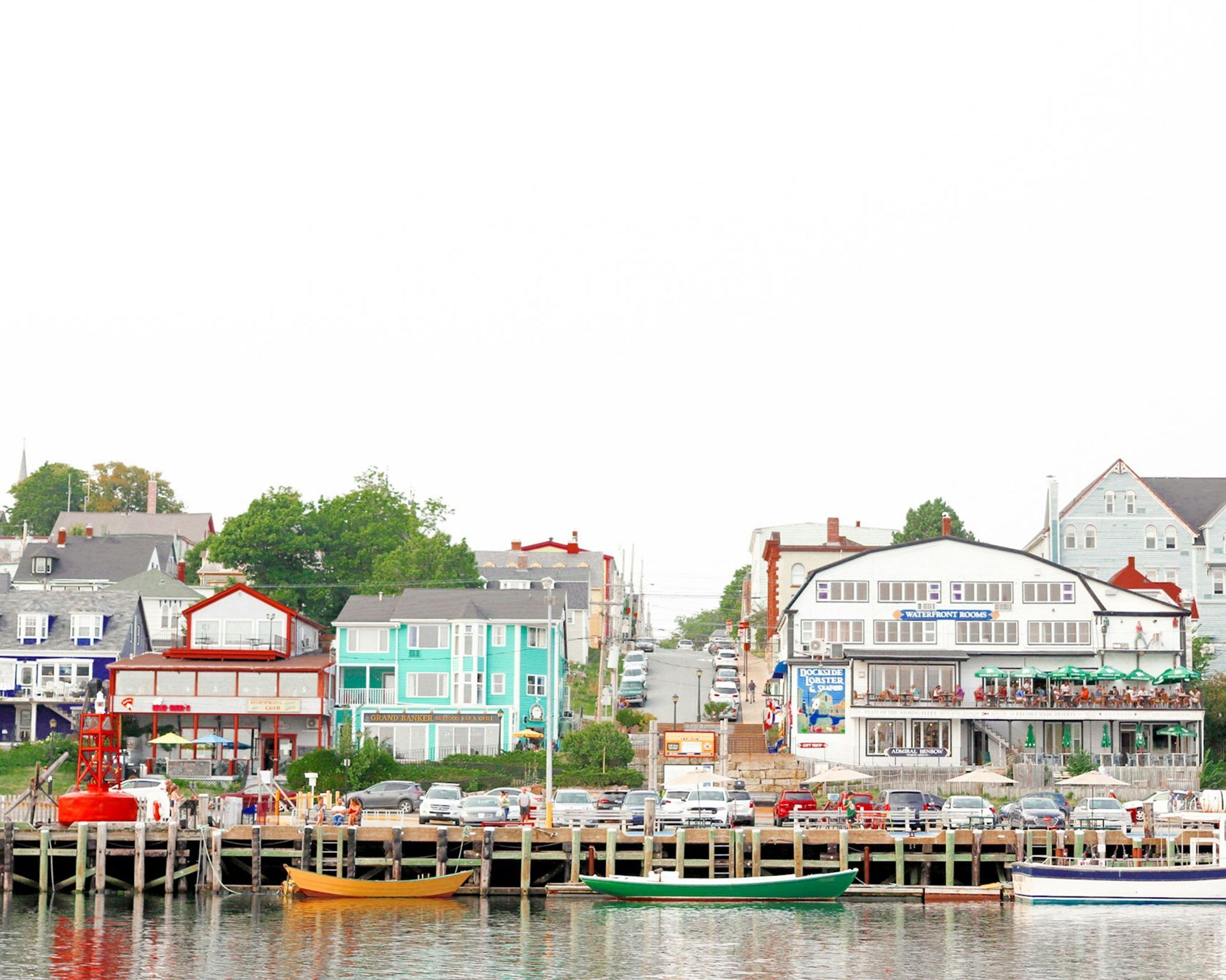 Waterfront view of a coastal town with colorful buildings, docks, boats, and a red buoy in Nova Scotia, Canada.