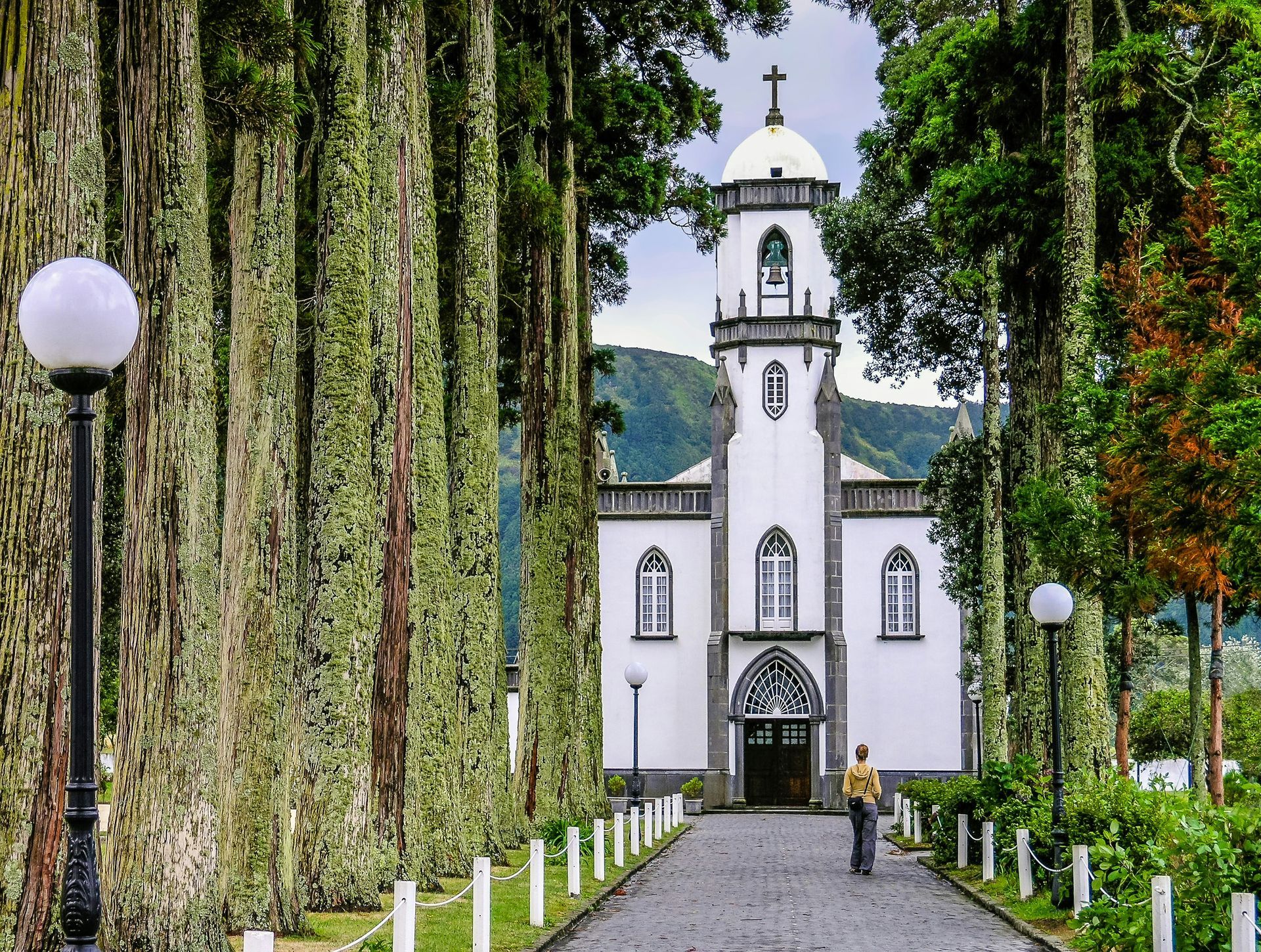 White church framed by trees, path leading to entrance, person walking away on the island of Azores, Portugal.